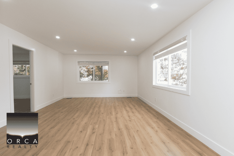 Spacious modern living room with hardwood floors and large windows in a new Orca Realty listing, perfect for homebuyers in Canada.