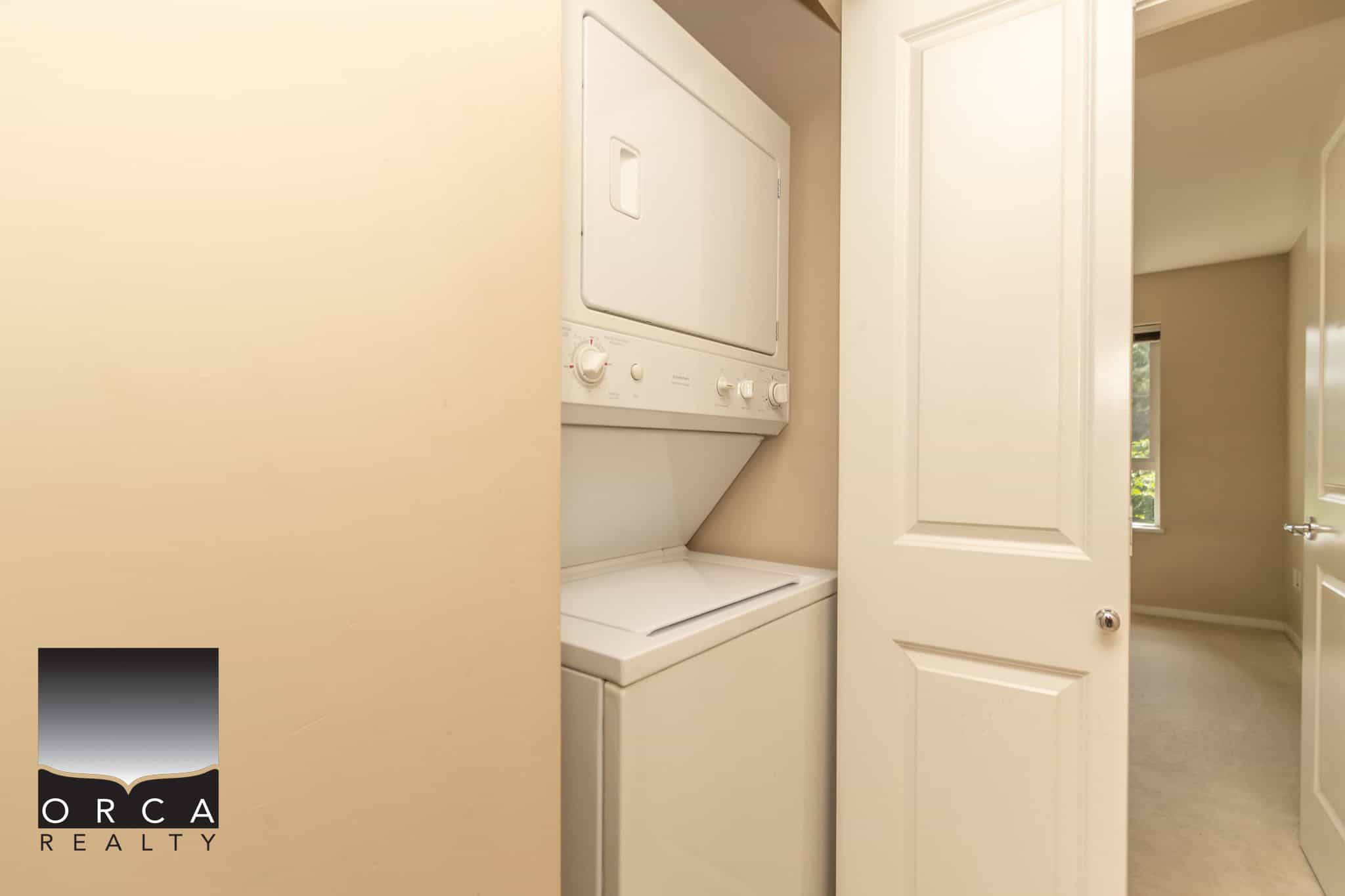 Stacked washer and dryer in a small laundry closet inside a home, with neutral beige walls and white door. Perfect for compact living, demonstrating functional laundry space in a modern residential interior.