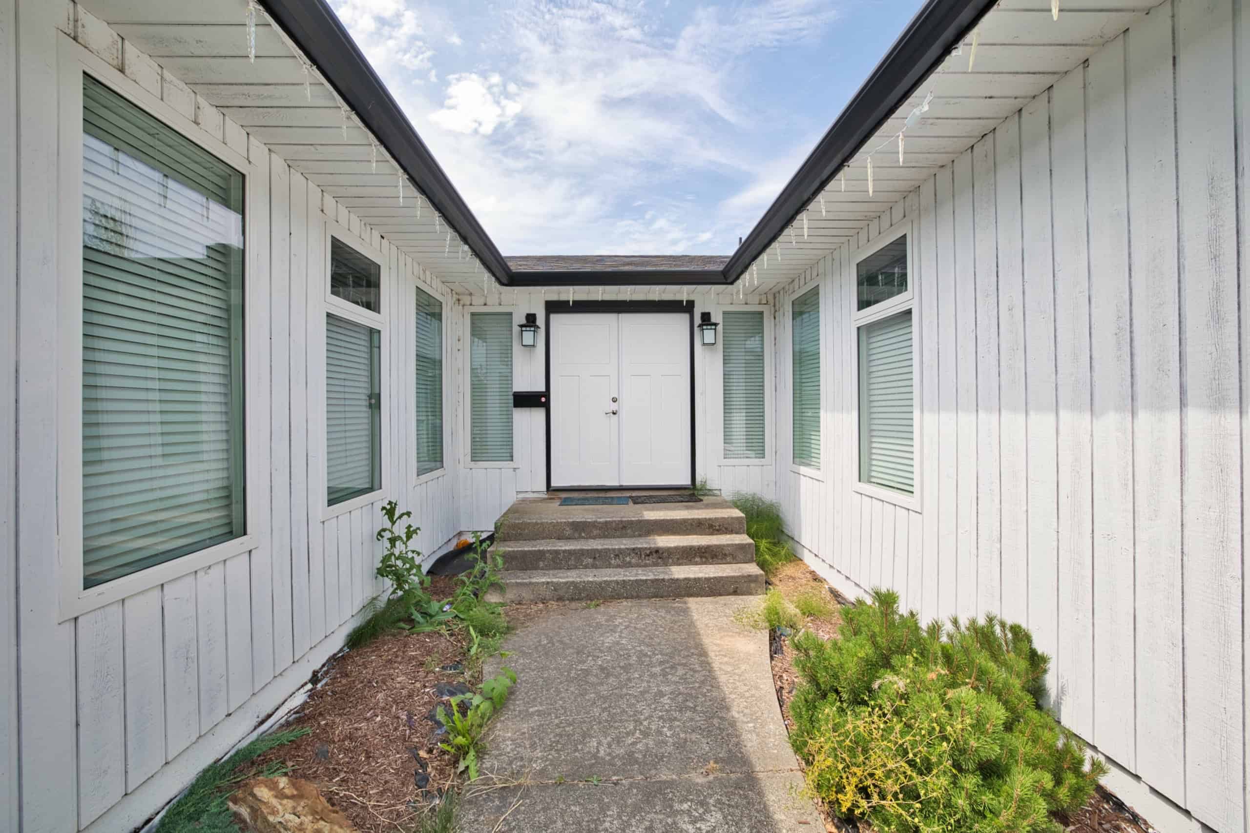 Bright white exterior of a modern house with large windows, a clean entryway, and steps leading up to a secure front door, perfect for Canadian residential real estate.