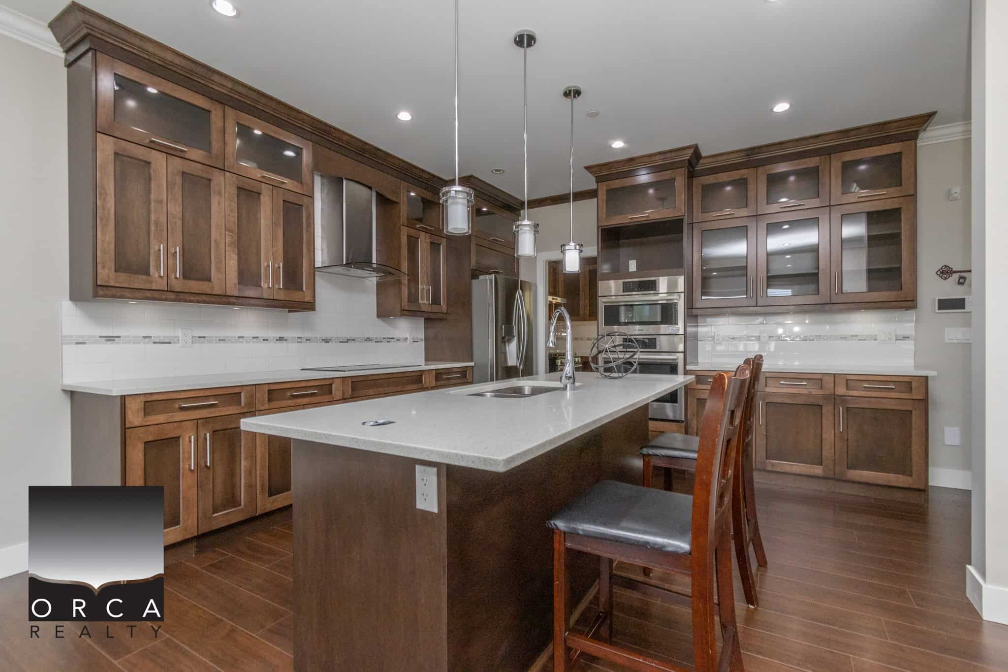 Modern kitchen with dark wood cabinets, white quartz countertops, stainless steel appliances, and a spacious island, ideal for Vancouver Island real estate listings.