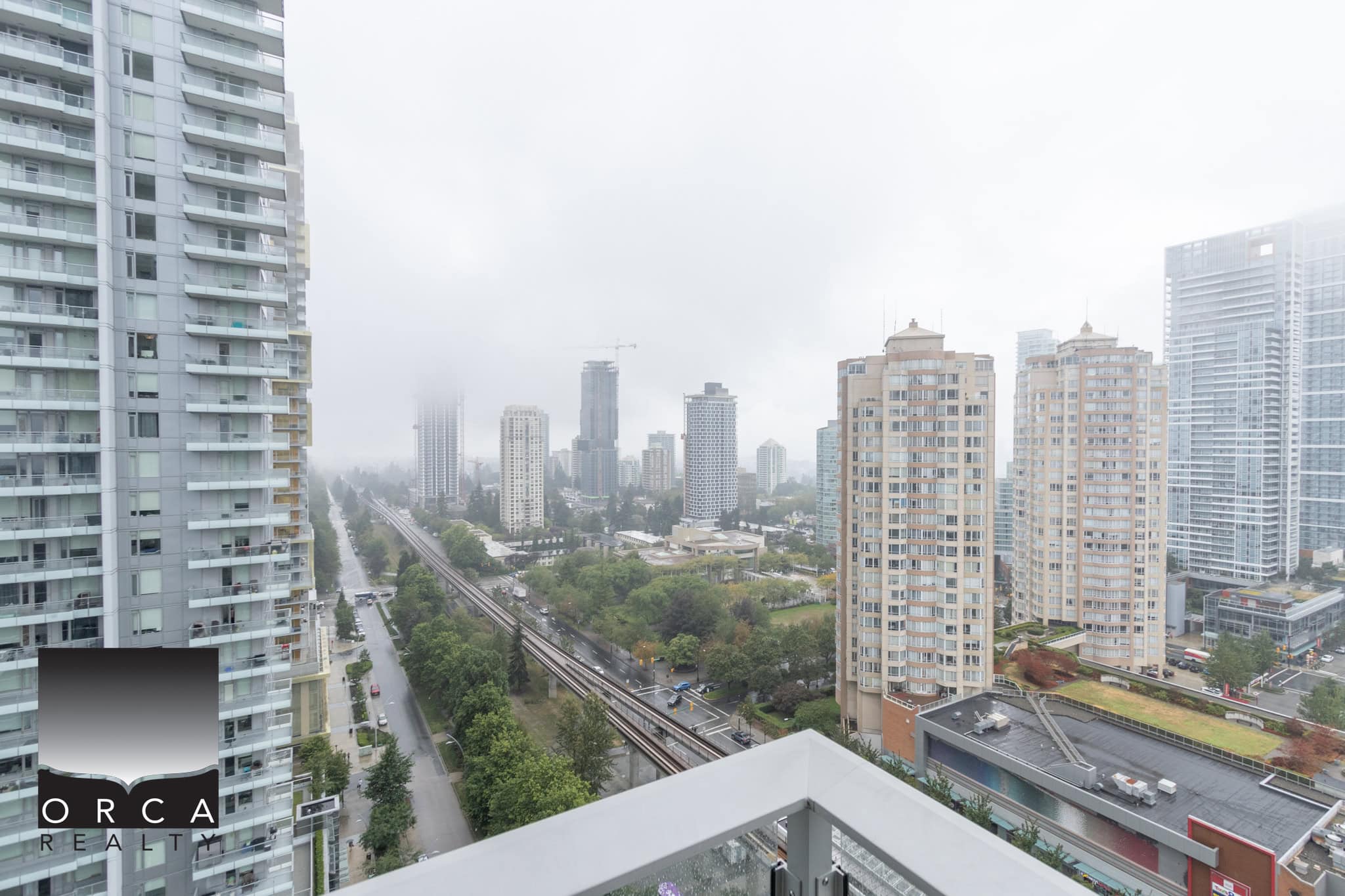 Panoramic view of Toronto skyline from a high-rise balcony, showcasing modern downtown buildings, city streets, and green parks on a cloudy day, ideal for Toronto real estate and condo living.