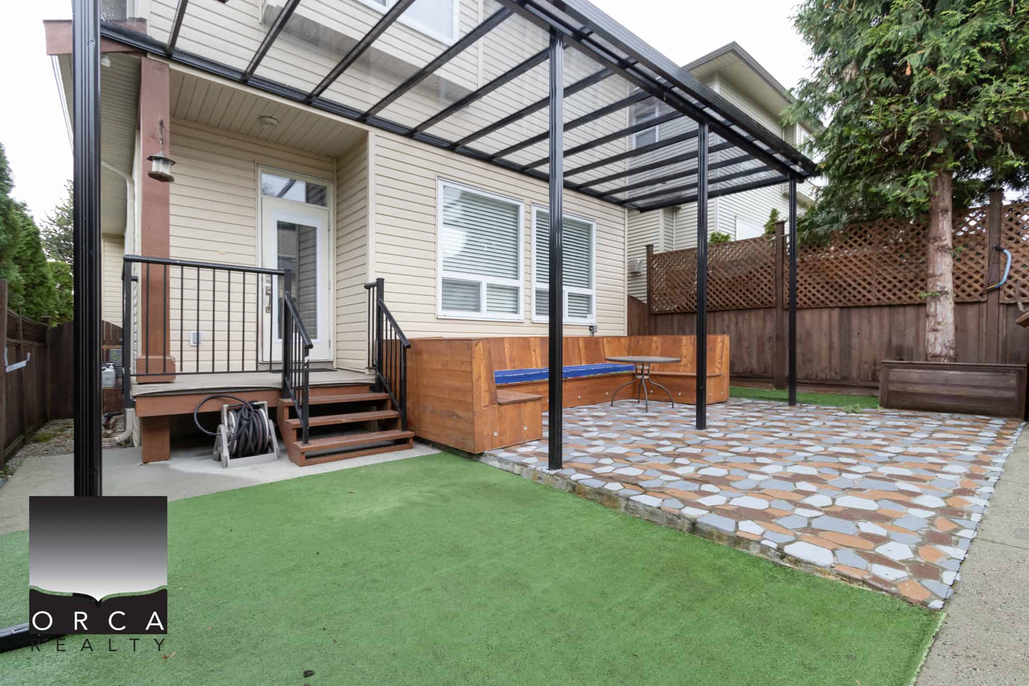 Modern backyard outdoor space with a covered patio, wooden steps, and decorative pavers, ideal for relaxing or entertaining, showcasing quality real estate in Orca Realty's property listings.