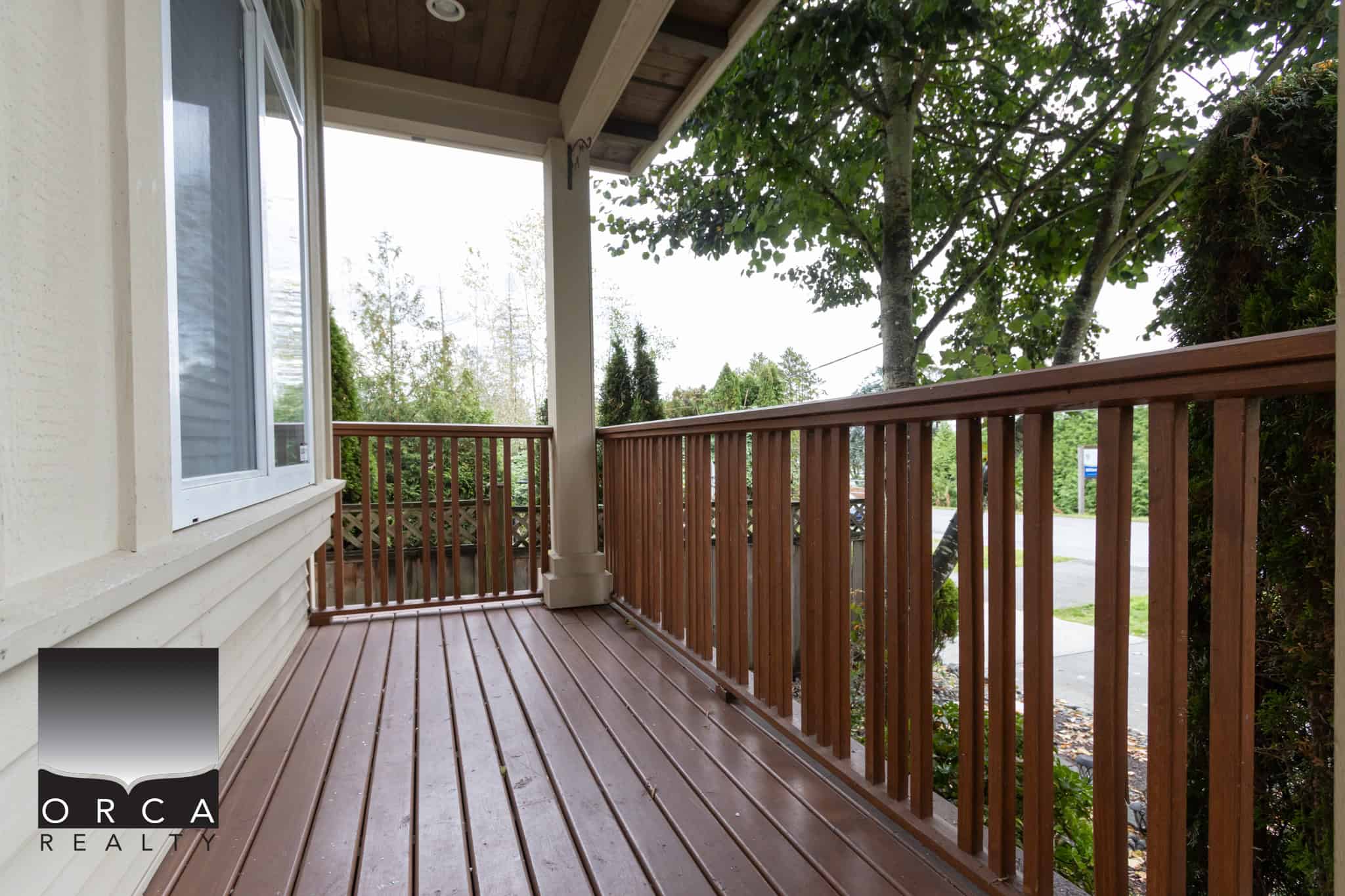 Spacious wooden front porch with a safety railing, nestled among lush trees, ideal for relaxation and enjoying the outdoor scenery. Perfect for potential homeowners and real estate listings.