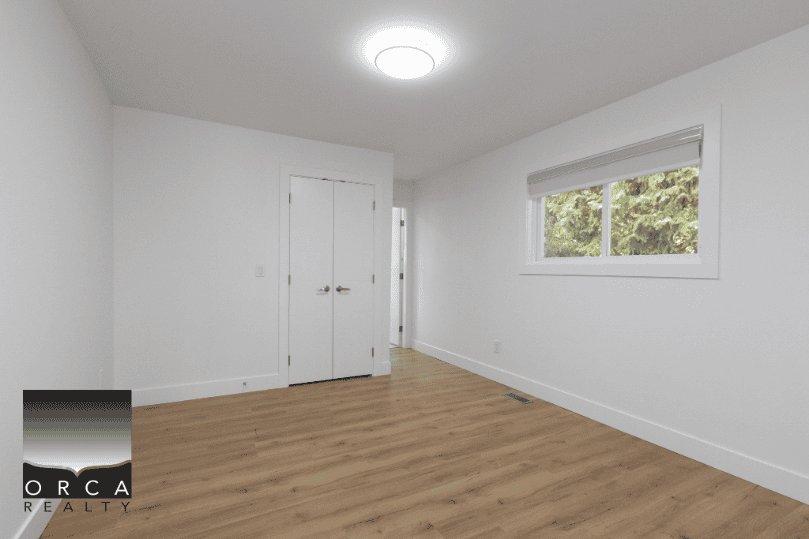 White empty room with hardwood floors, large window, and modern lighting - Orca Realty Inc. for Vancouver & Lower Mainland real estate services.