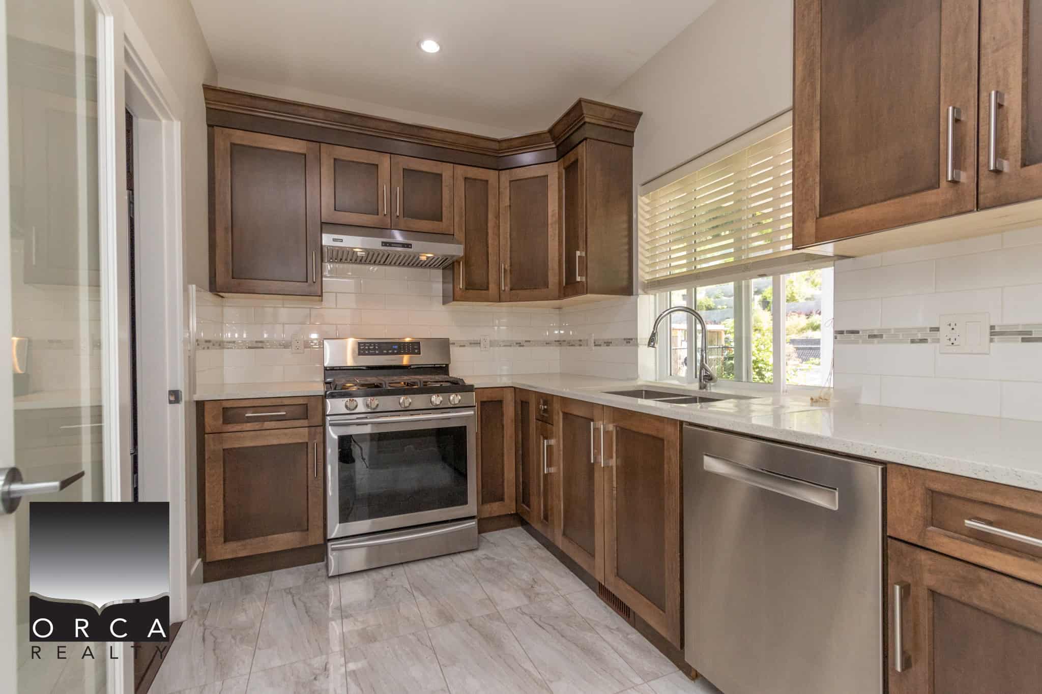 Bright modern kitchen with wooden cabinets, stainless steel appliances, and a large window with blinds, ideal for homeowners seeking a stylish and functional culinary space.