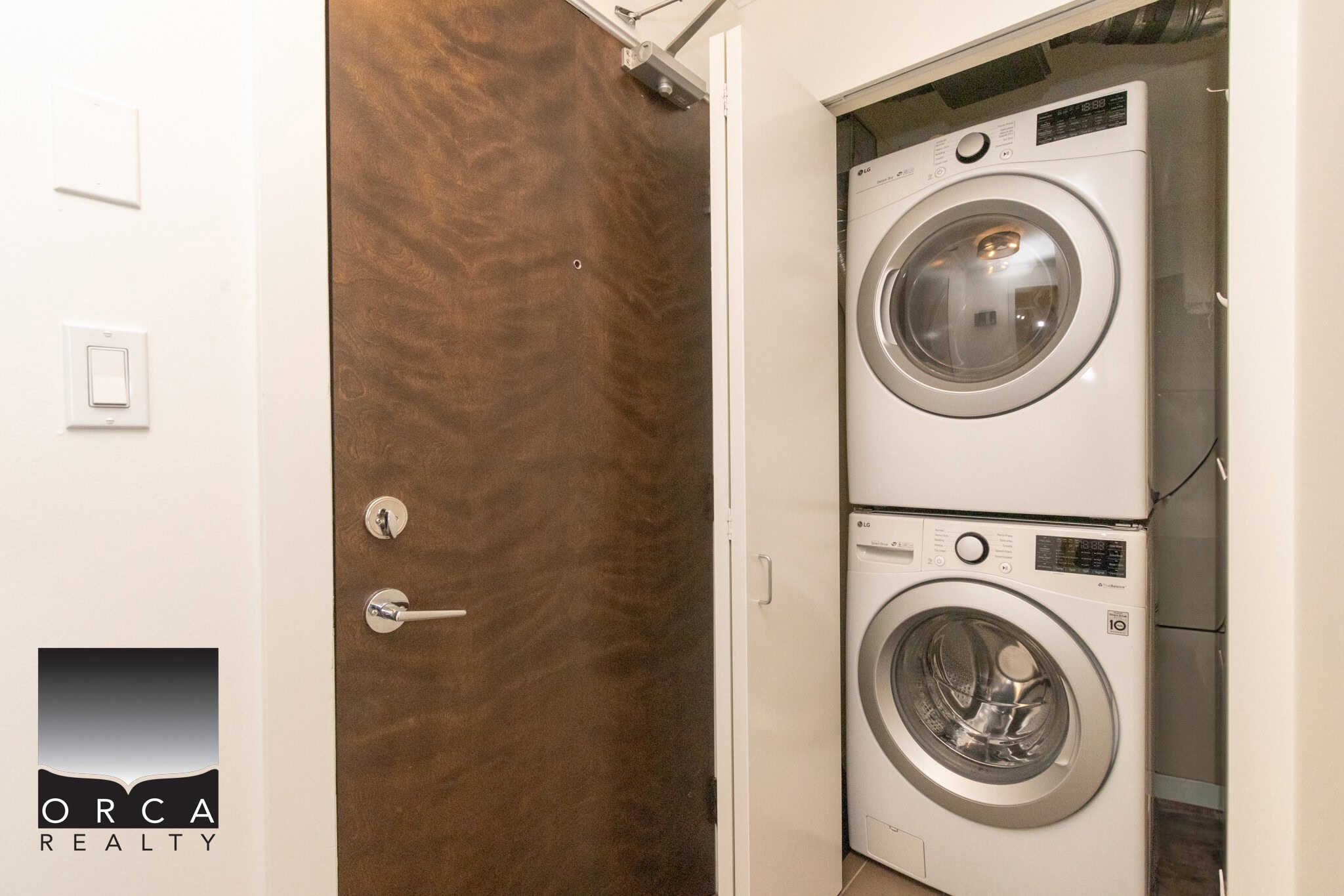 Stacked washer and dryer in a compact laundry closet with white walls and a wooden door, perfect for modern home storage solutions.