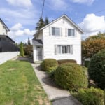 Charming white two-storey home with manicured front yard and lush greenery, located in a desirable neighbourhood, ideal for buyers seeking a cozy residence and investment property in Vancouver.