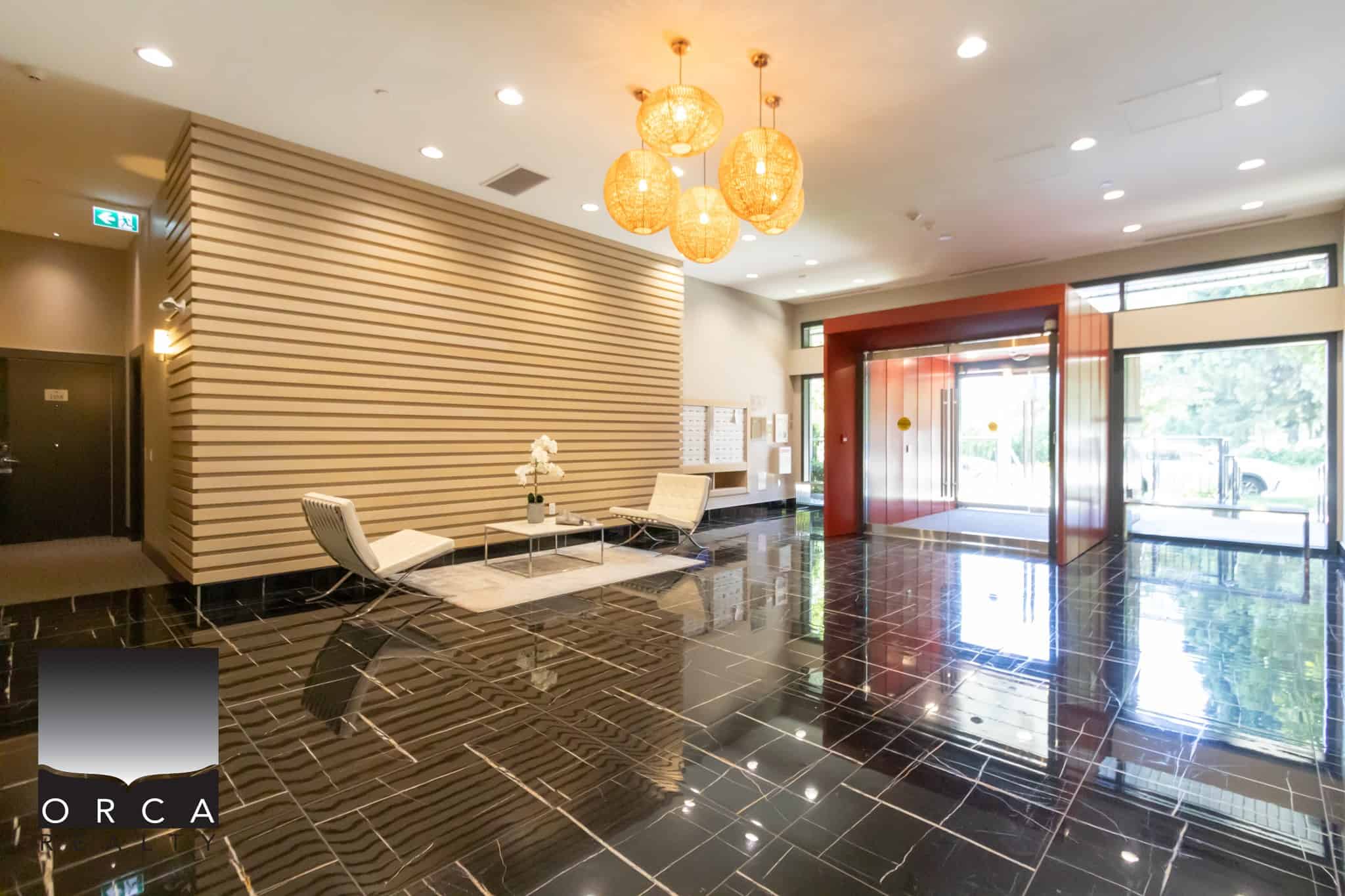 Modern condominium lobby with elegant seating area, contemporary lighting, and sleek black tile flooring, showcasing Orca Realty Inc.'s professional property management services in Vancouver, BC.