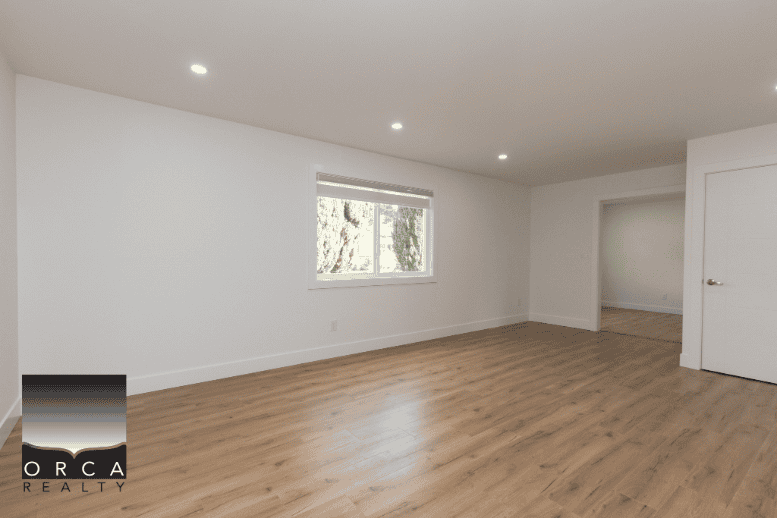 Bright and spacious empty living room with large window, hardwood flooring, and modern lighting, ideal for Vancouver area real estate listings.