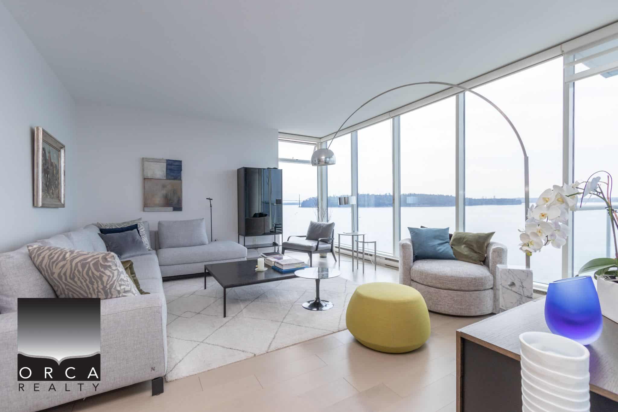 Luxurious waterfront living room with floor-to-ceiling windows showcasing stunning water views, modern decor, and spacious interior featuring stylish sofas, contemporary furniture, and elegant accessories.