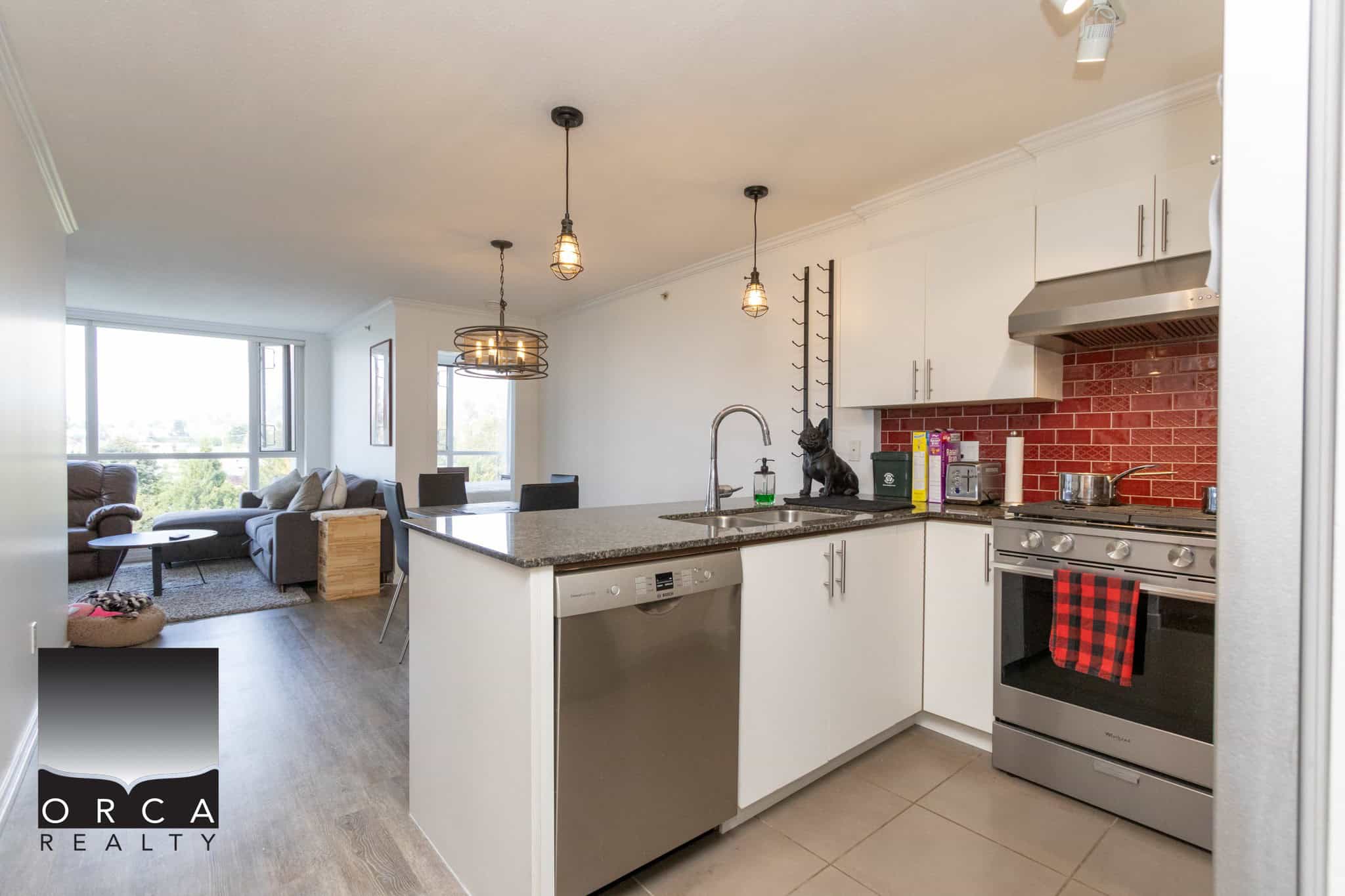 Bright modern kitchen with stainless steel appliances, red brick backsplash, white cabinetry, and open-concept living space in Vancouver.