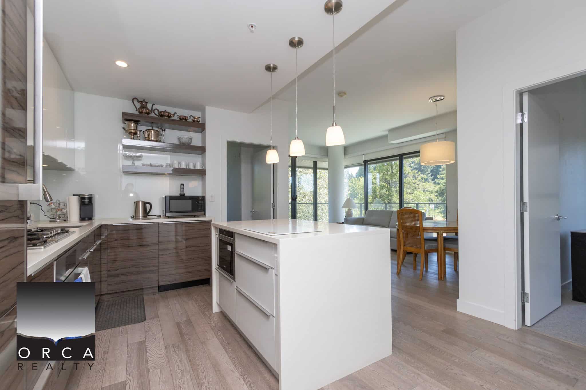 Modern open-concept kitchen with sleek wood cabinetry, white countertops, and stainless steel appliances, perfect for Vancouver homebuyers seeking contemporary condo or apartment living.