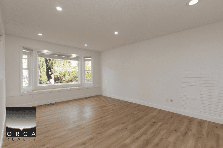Spacious empty living room with large bay window, white walls, and hardwood flooring, ideal for Vancouver-area real estate buyers.