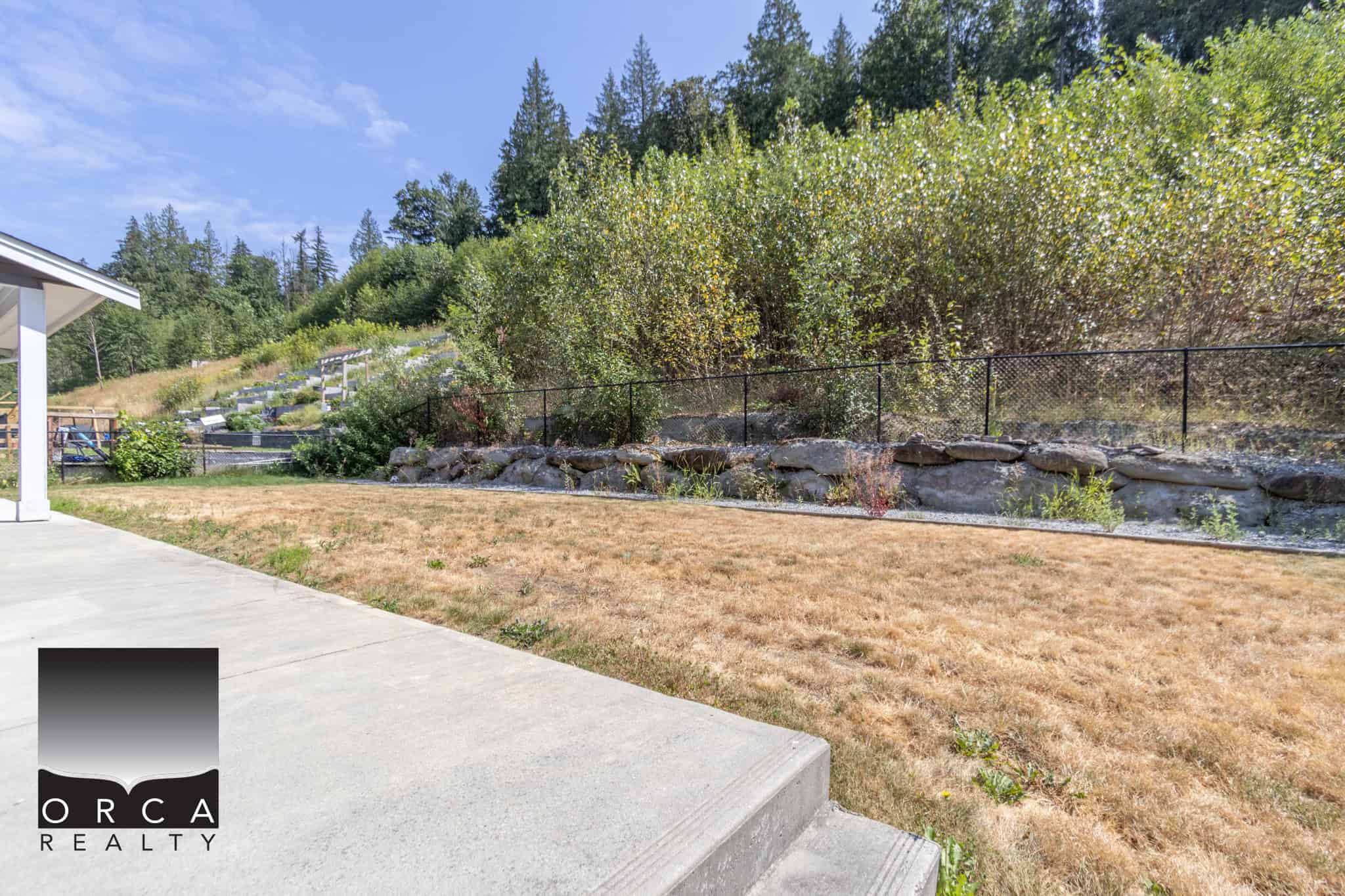 Lush backyard with a landscaped garden, stone retaining wall, and scenic mountain views from Orca Realty Inc. trusted Vancouver Island real estate experts.