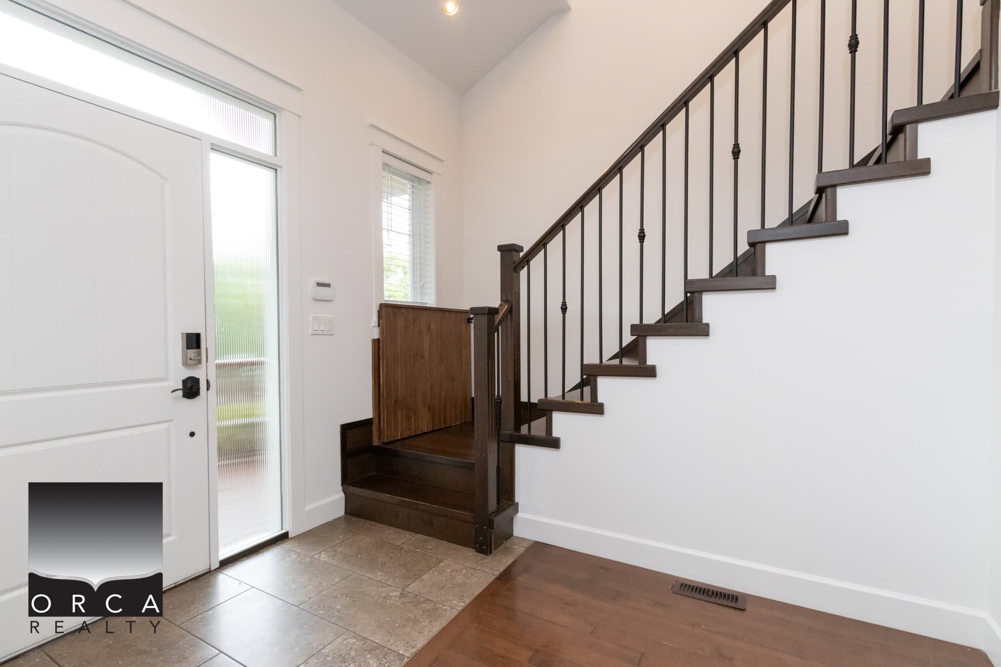 Modern entryway with staircase, wooden flooring, and natural light, showcasing a welcoming home interior by Orca Realty Inc.