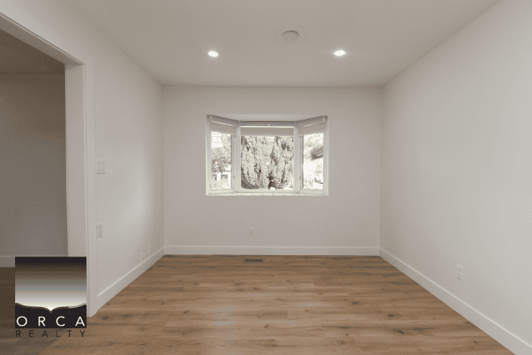 Bright empty room with hardwood flooring and large window, in a residential property listed by Orca Realty Inc.
