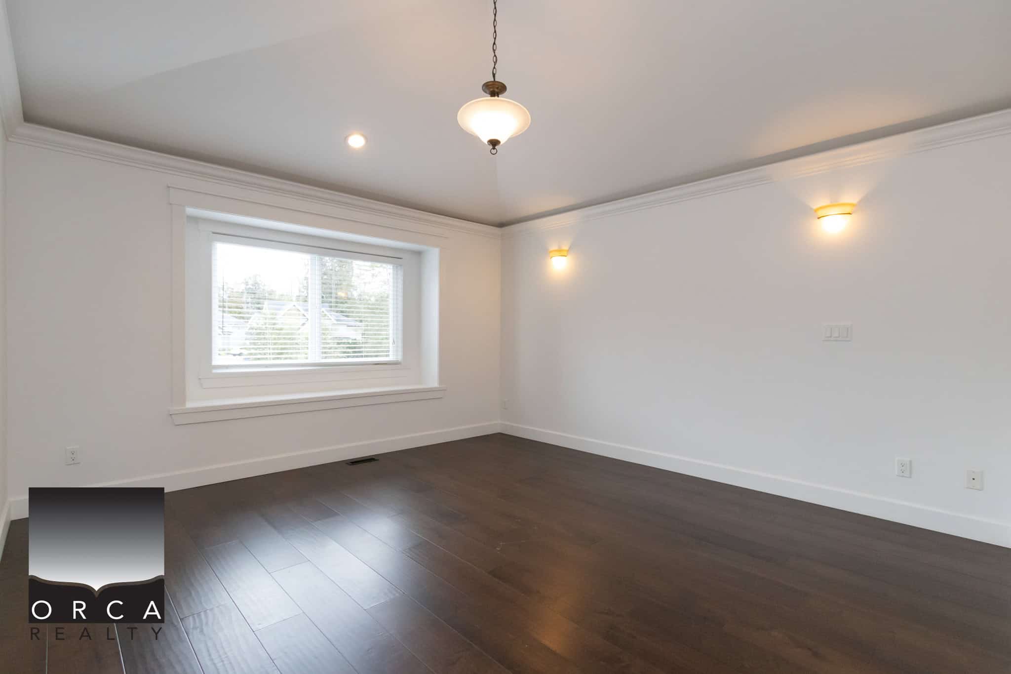 Bright empty living room with large window, white walls, dark hardwood floor, ceiling light fixture, and modern wall sconces, ideal for Vancouver homebuyers.