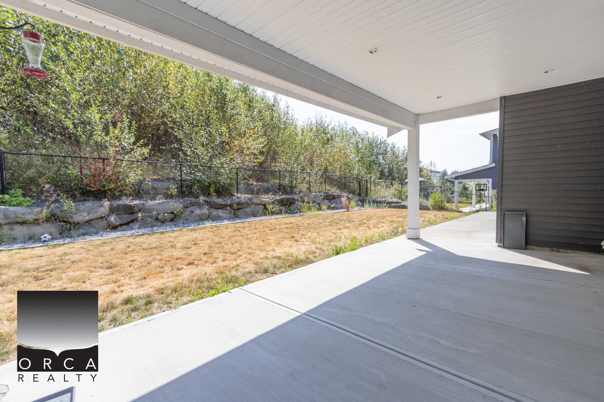 Spacious backyard patio with a covered area, lush greenery, and a rock garden, perfect for outdoor living and entertaining in a Vancouver Island home.