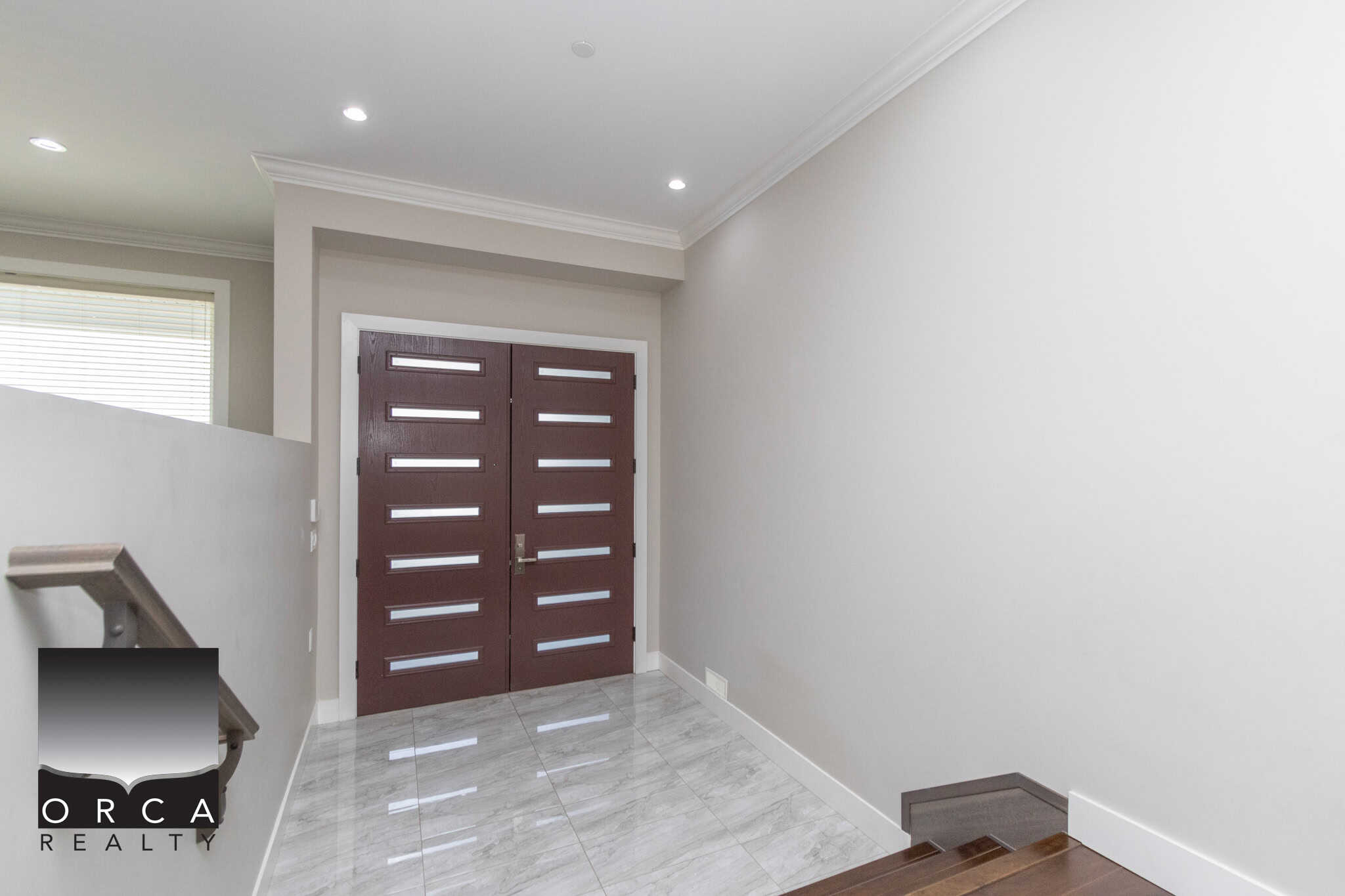 Contemporary home entrance with stylish double wooden doors, modern white walls, and polished tile flooring, showcasing Orca Realty Inc.'s expertise in Vancouver Island real estate.