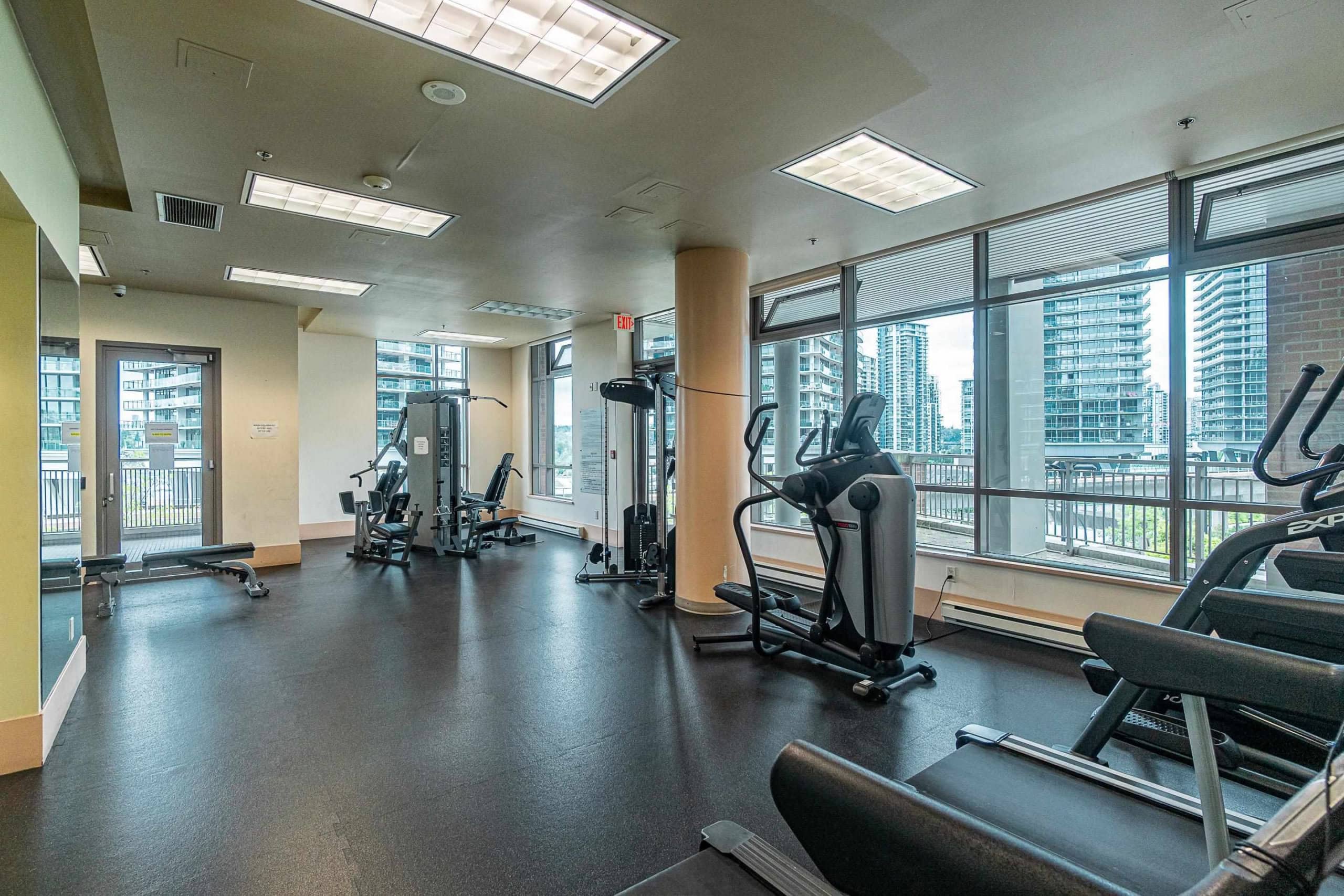 Modern urban gym with cardio and strength equipment, large windows with city skyline views, ideal for fitness at Orca Realty Inc.