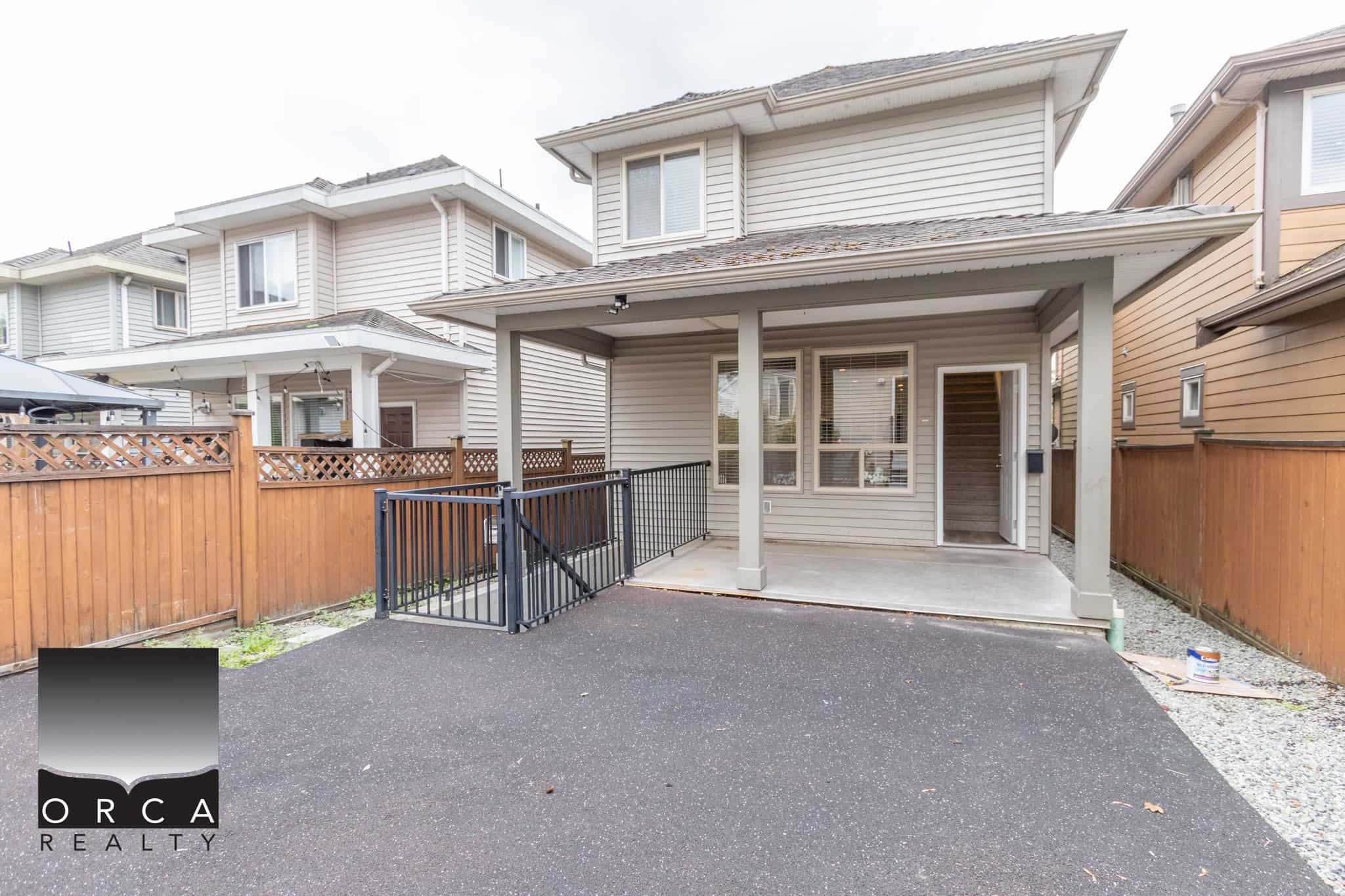 Bright backyard patio of a modern townhouse, featuring a covered porch, black metal railing, and freshly paved asphalt, ideal for outdoor living and entertaining in Vancouver real estate.