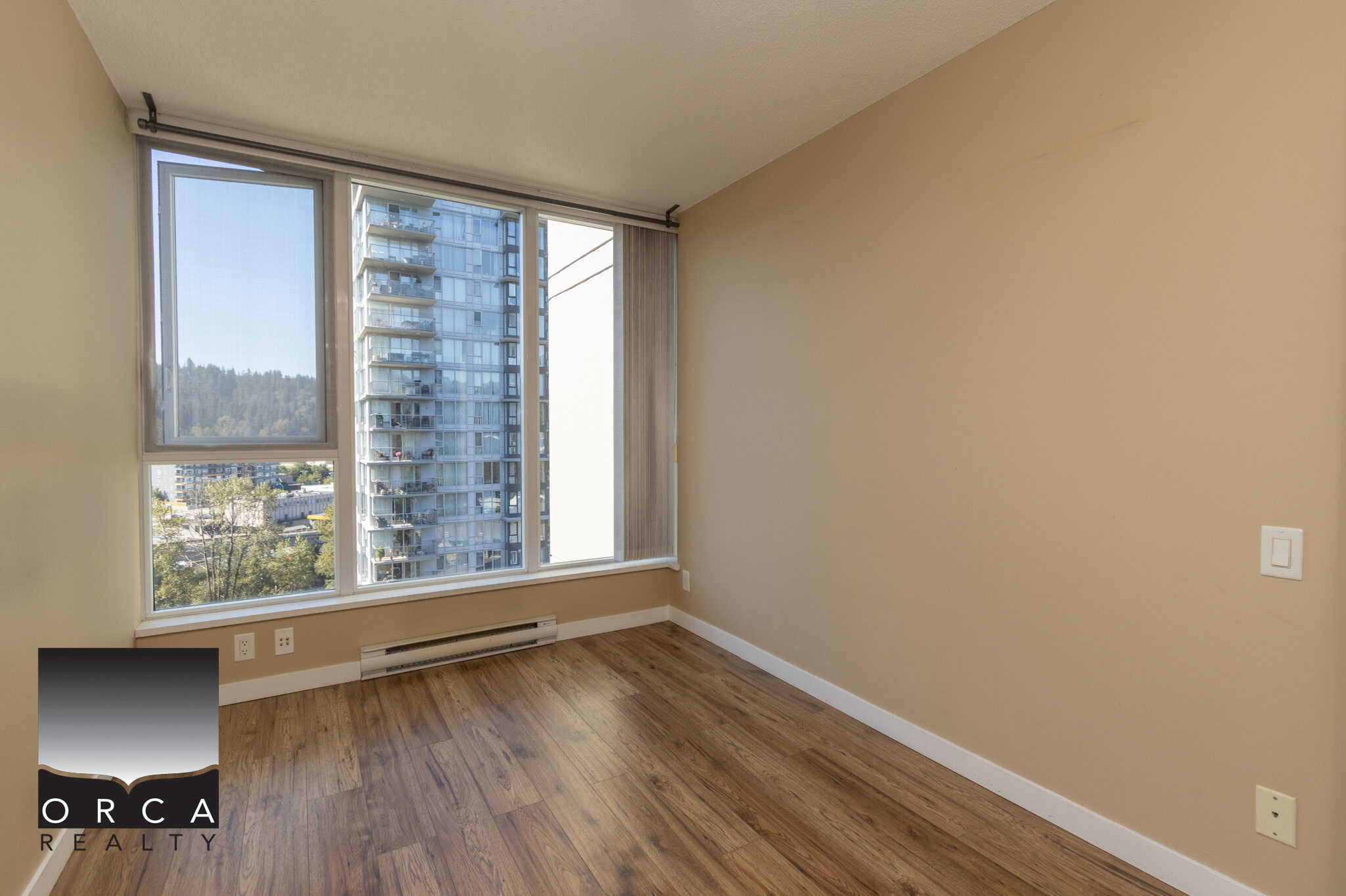 Bright, unfurnished city-view apartment bedroom with large window, beige walls, and hardwood flooring, ideal for Vancouver real estate buyers seeking modern condo living near downtown and natural surroundings.