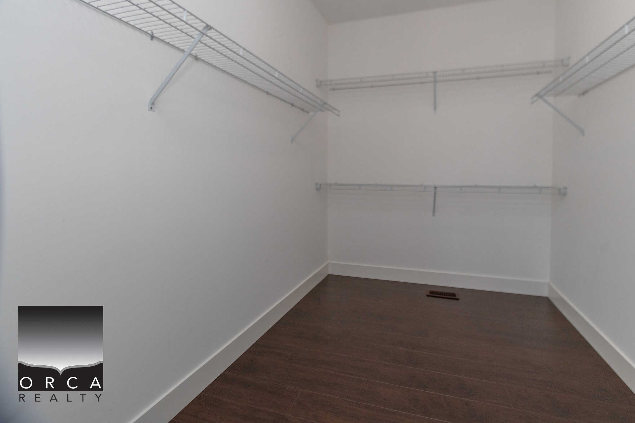 Spacious walk-in closet with white wire shelves, dark hardwood flooring, and neutral walls, ideal for organizing and storage in a modern home.