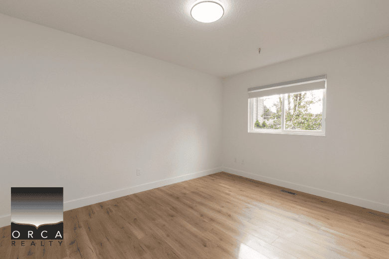 Bright empty bedroom with white walls, large window, and hardwood flooring, ideal for Vancouver homeowners seeking professional real estate services.