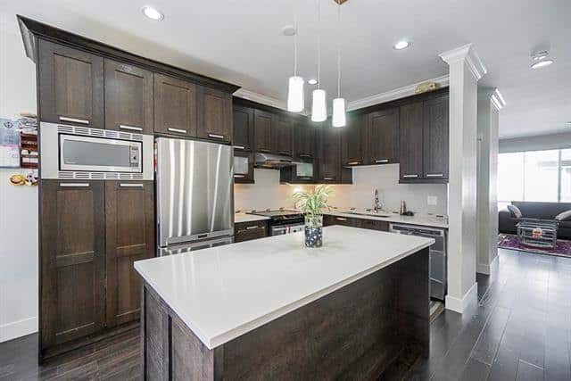 Kitchen with dark wood cabinets and white countertop island in a modern home, featuring stainless steel appliances and ample natural light. Ideal for contemporary living in Victoria, BC.