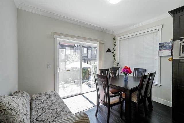 Modern dining area with a black table and six chairs, bright natural light from large windows and sliding glass door, cozy home interior, perfect for family gatherings or entertaining guests.