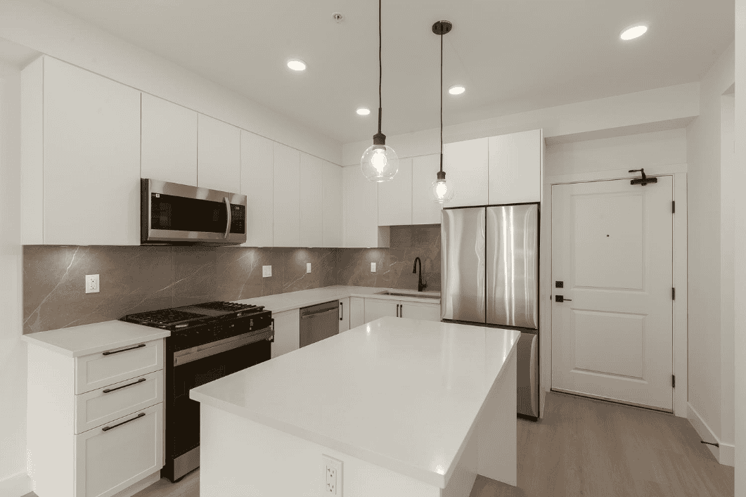 Bright modern white kitchen with stainless steel appliances, sleek cabinetry, and contemporary pendant lighting, ideal for Vancouver real estate buyers seeking stylish homes.
