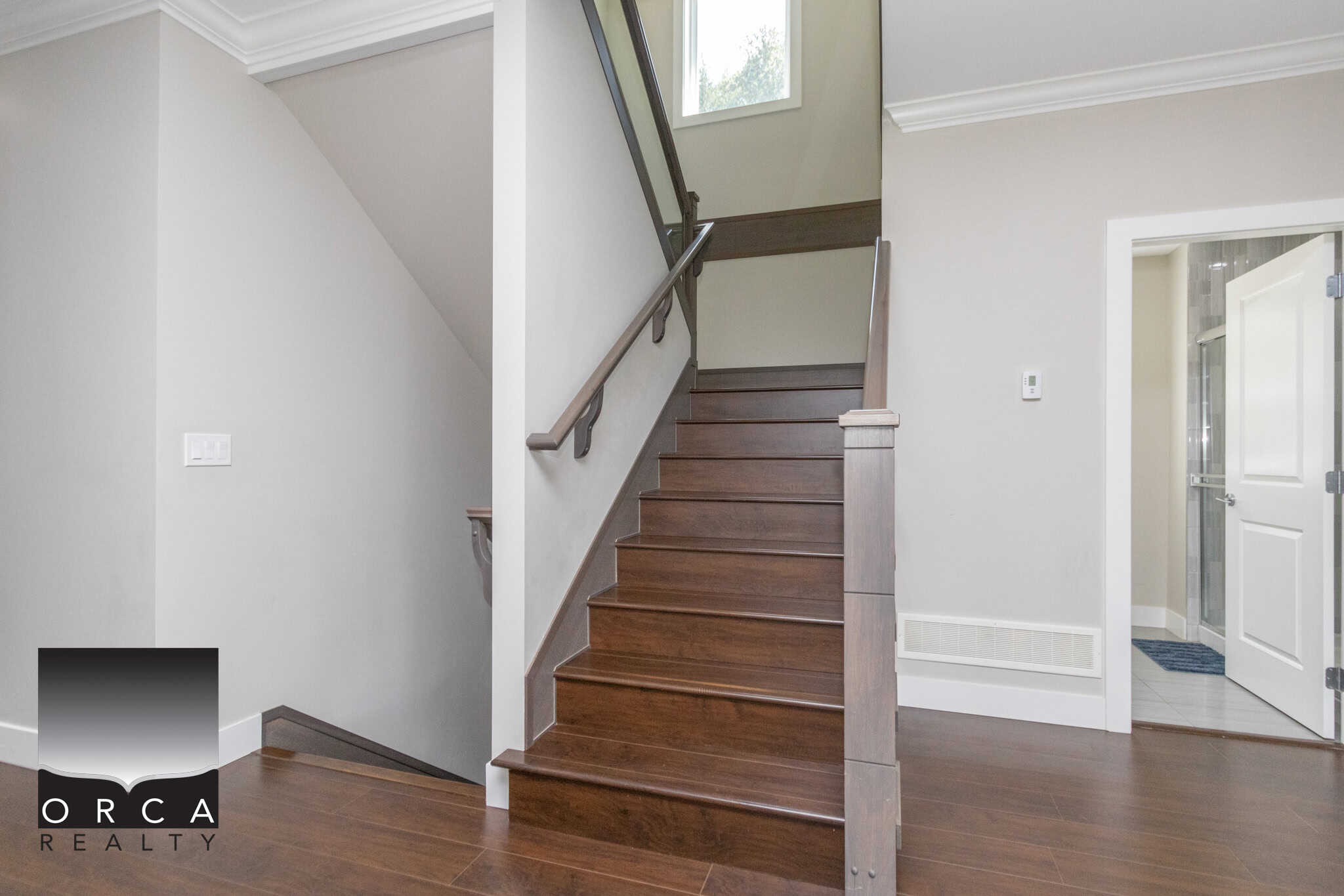 Modern interior staircase with dark wood steps and white walls, featuring natural light from window, showcasing Orca Realty Inc. expertise in Vancouver Island residential property listings and real estate services.