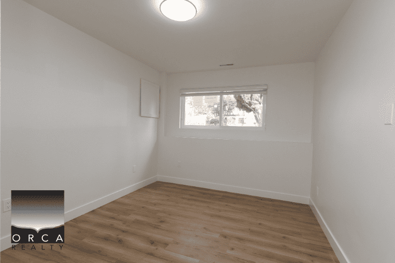 Bright empty bedroom with white walls, hardwood flooring, and a large window, showcasing a modern interior suitable for Vancouver real estate listings.