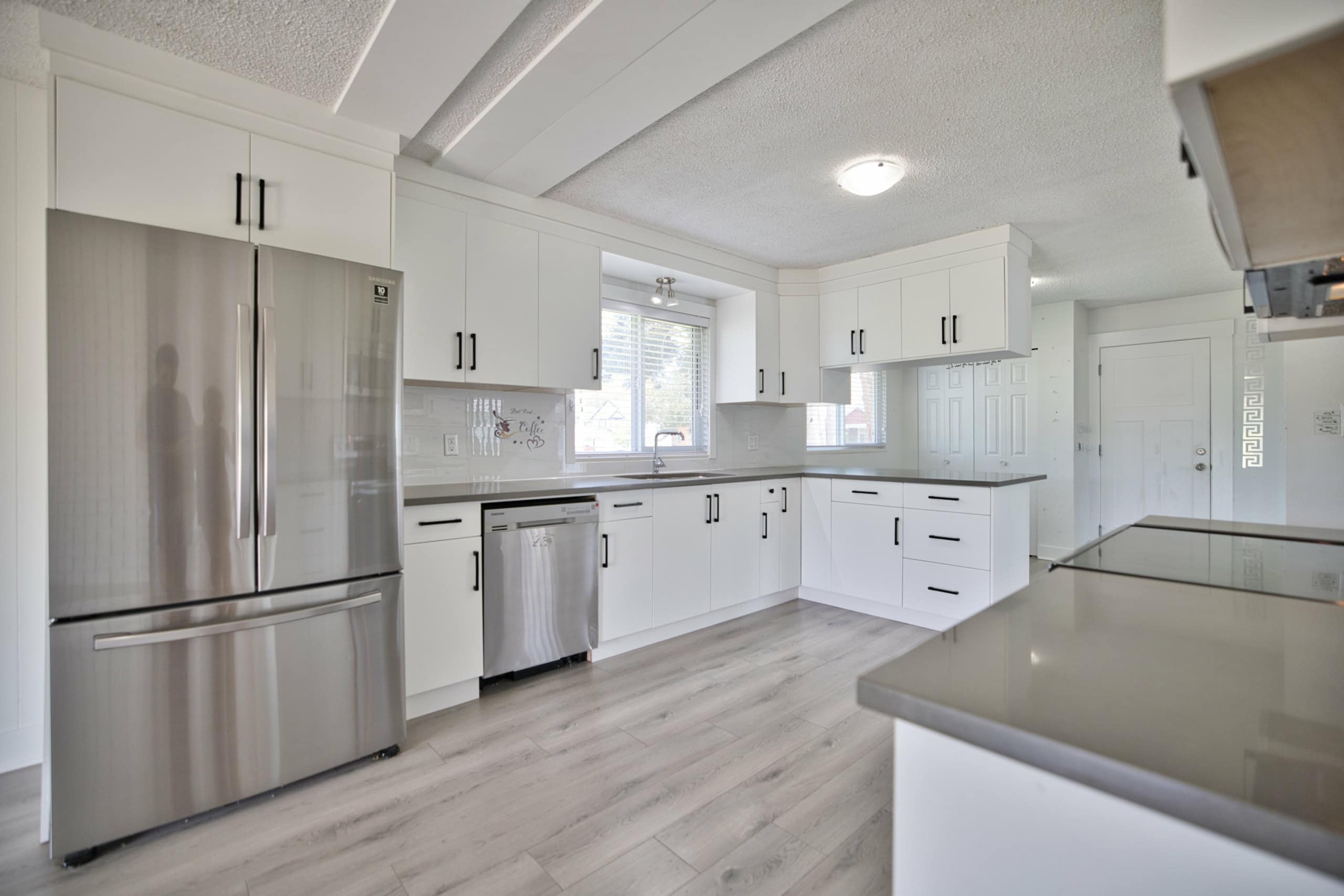 Modern white kitchen with stainless steel appliances, ample cabinet storage, and large windows for natural light, ideal for Vancouver Island real estate and property buyers.