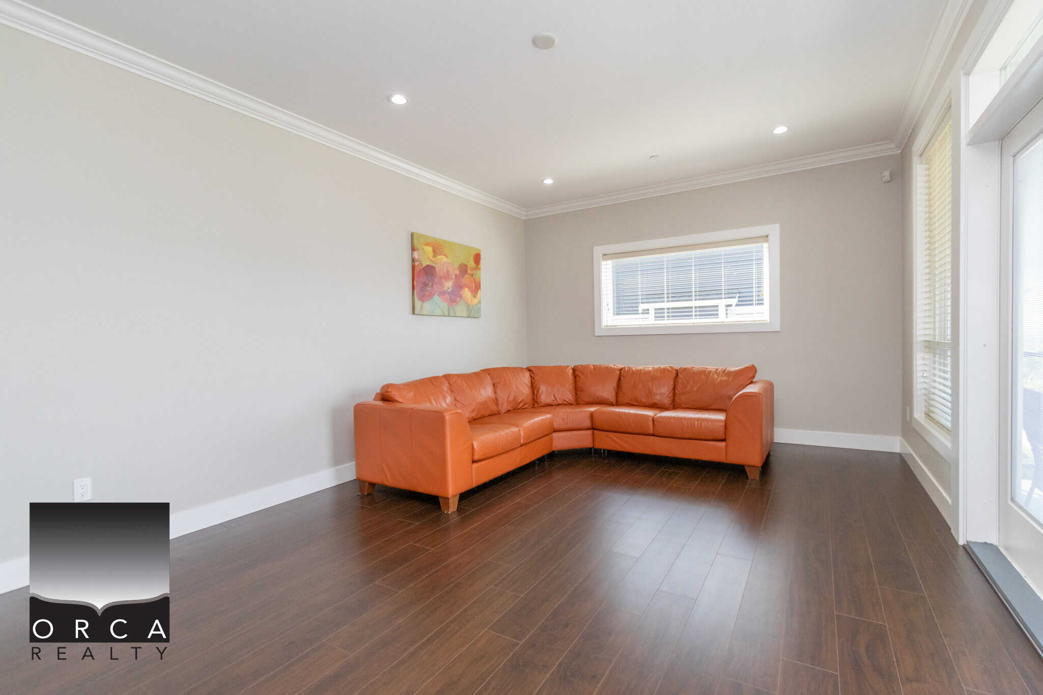 Bright living room with modern decor, featuring a spacious orange leather sofa, hardwood floors, and large windows offering ample natural light, perfect for Vancouver Island homebuyers.