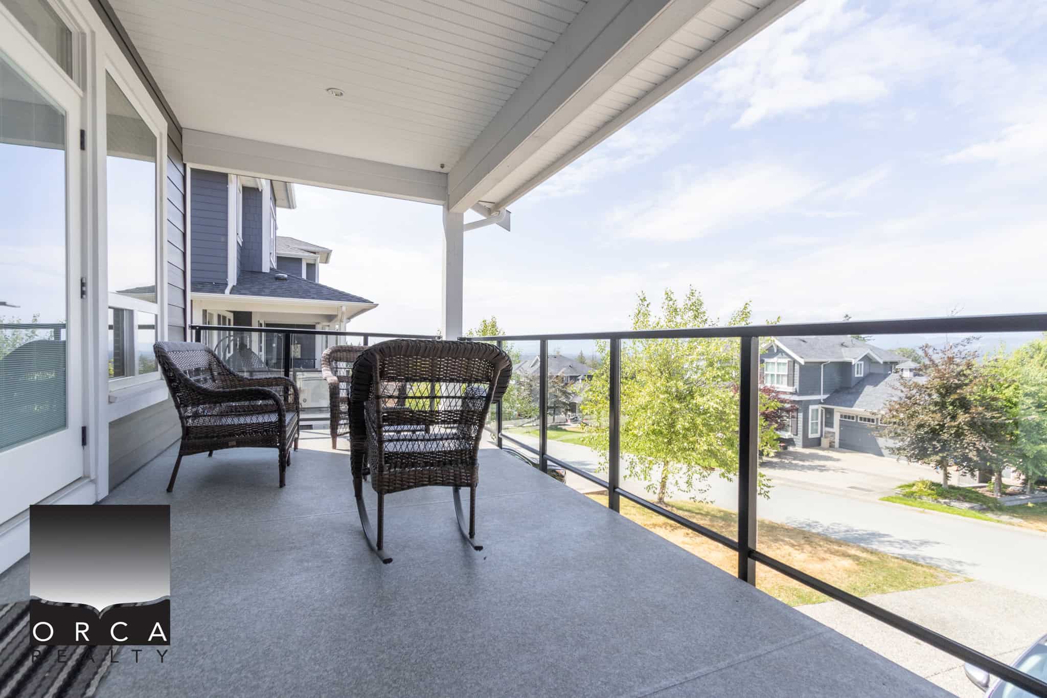 Spacious balcony with outdoor furniture overlooking a suburban neighbourhood on a sunny day.