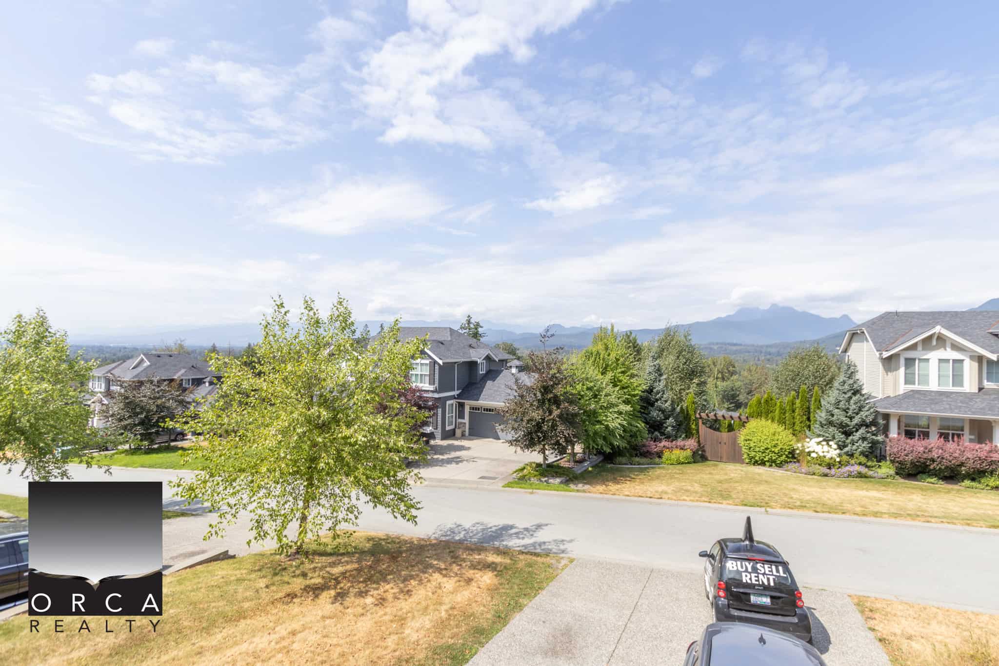 Beautiful suburban neighbourhood with spacious houses, lush trees, and scenic mountain views in the background, ideal for buying, selling, or renting real estate in the area.