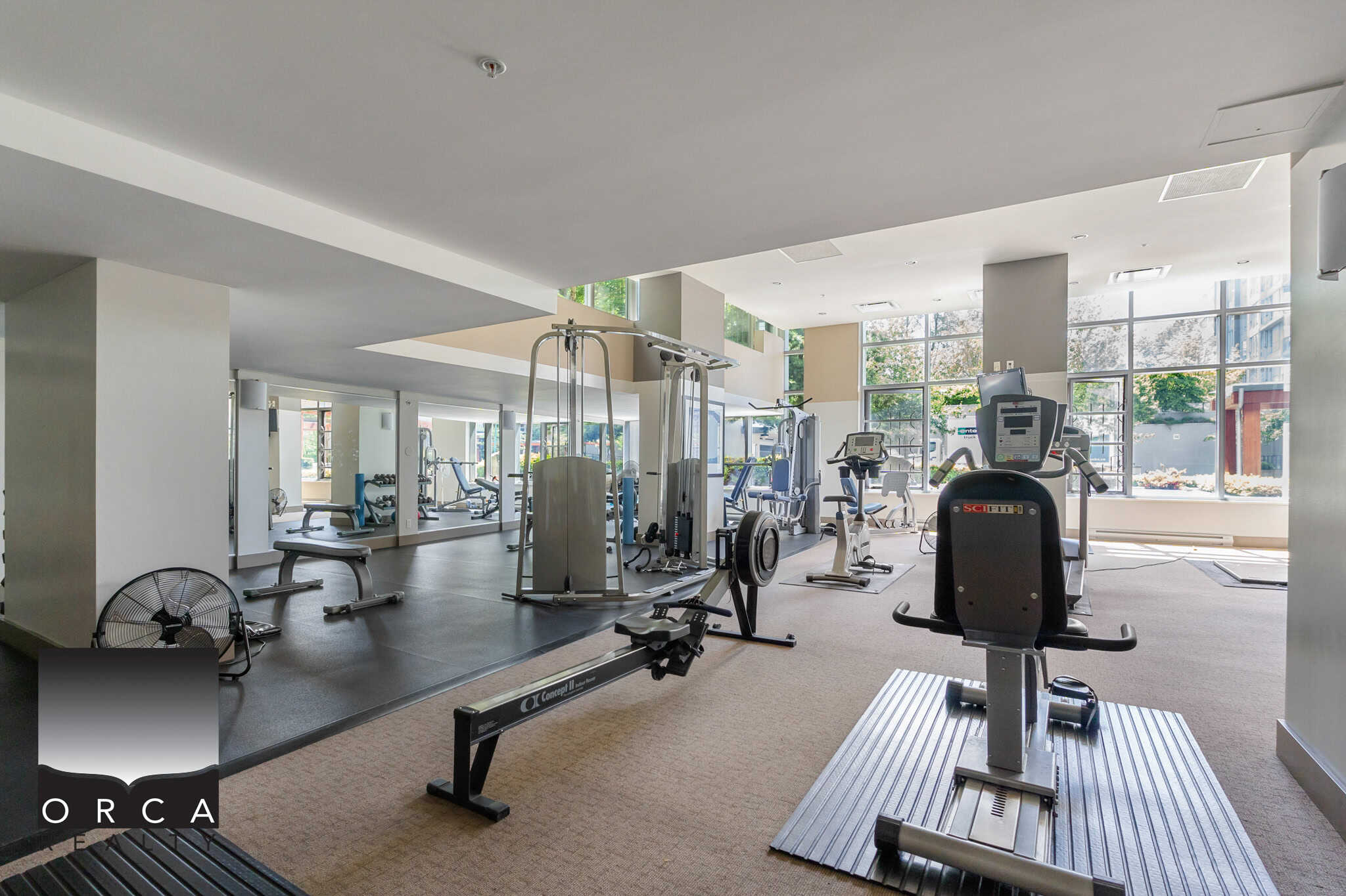 Modern indoor gym at Orca Realty Inc. featuring cardio equipment, strength training machines, and free weights to support a healthy lifestyle in a bright, spacious environment.