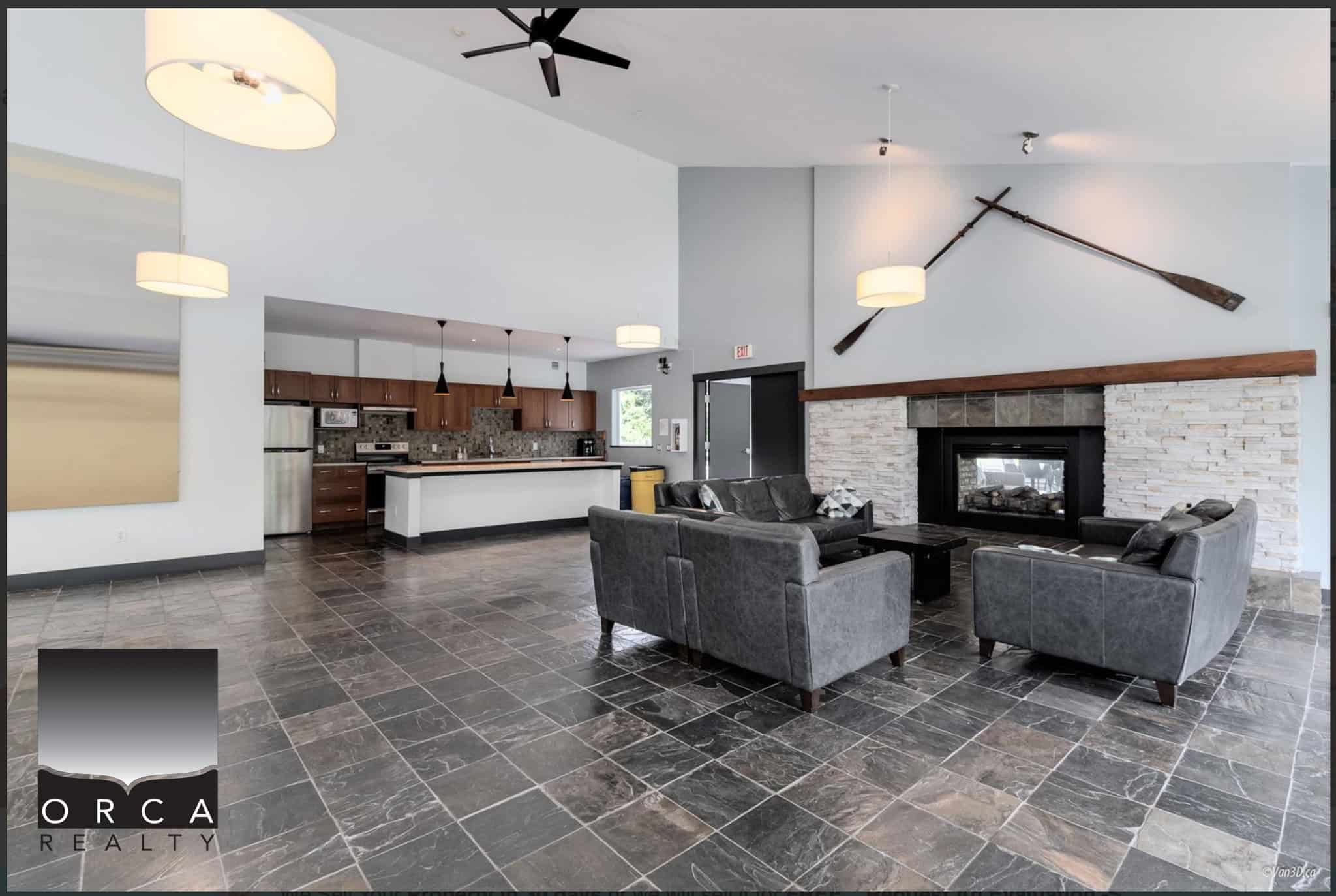 Modern living room with large stone fireplace and vaulted ceiling, open-concept kitchen, and stylish decor, showcasing Orca Realty Inc. services in Vancouver, BC.