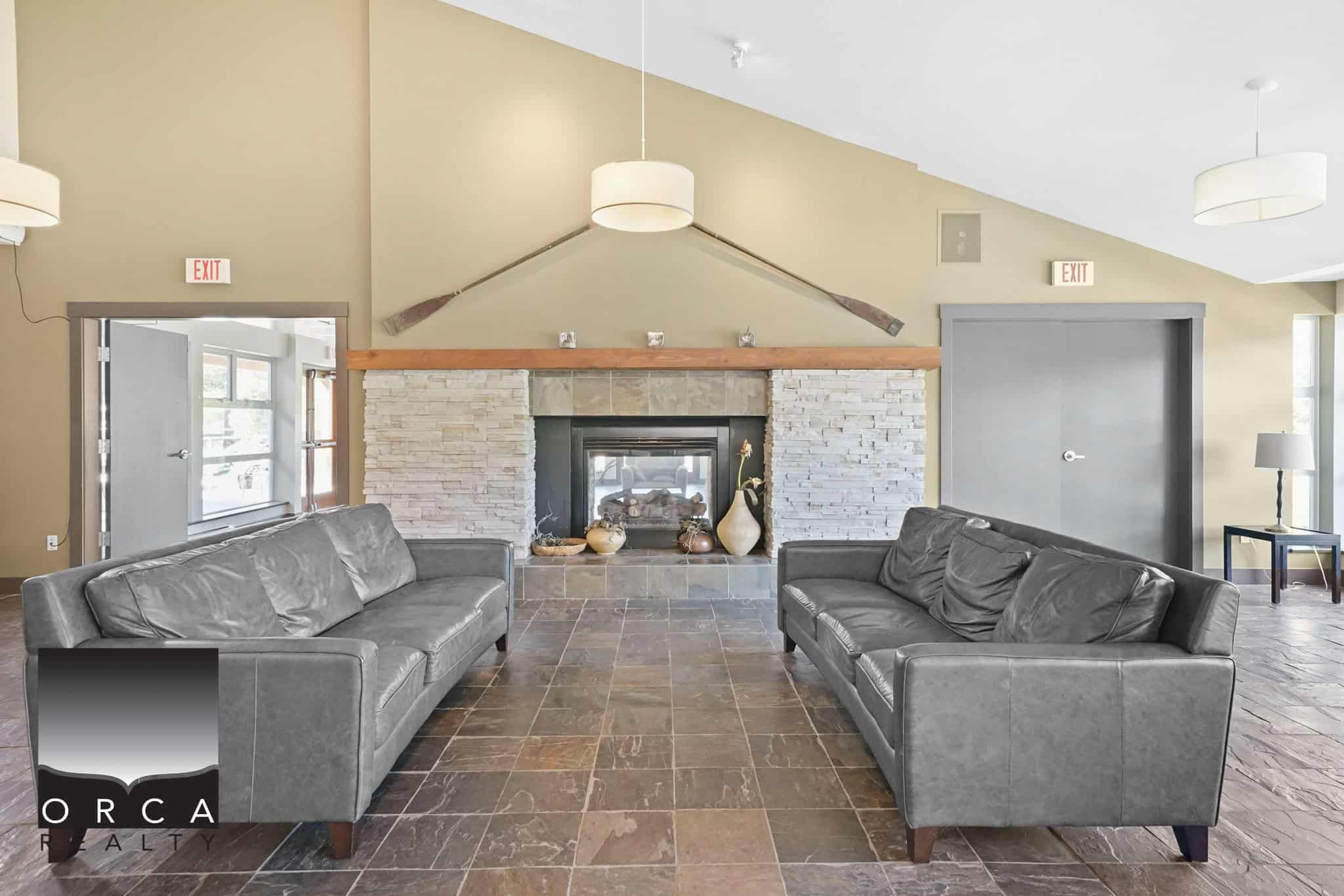 Cozy living room with stone fireplace, modern grey sofas, and rustic décor, showcasing Orca Realty Inc. property features and inviting interior design. Perfect for relaxed gatherings in a stylish home setting.