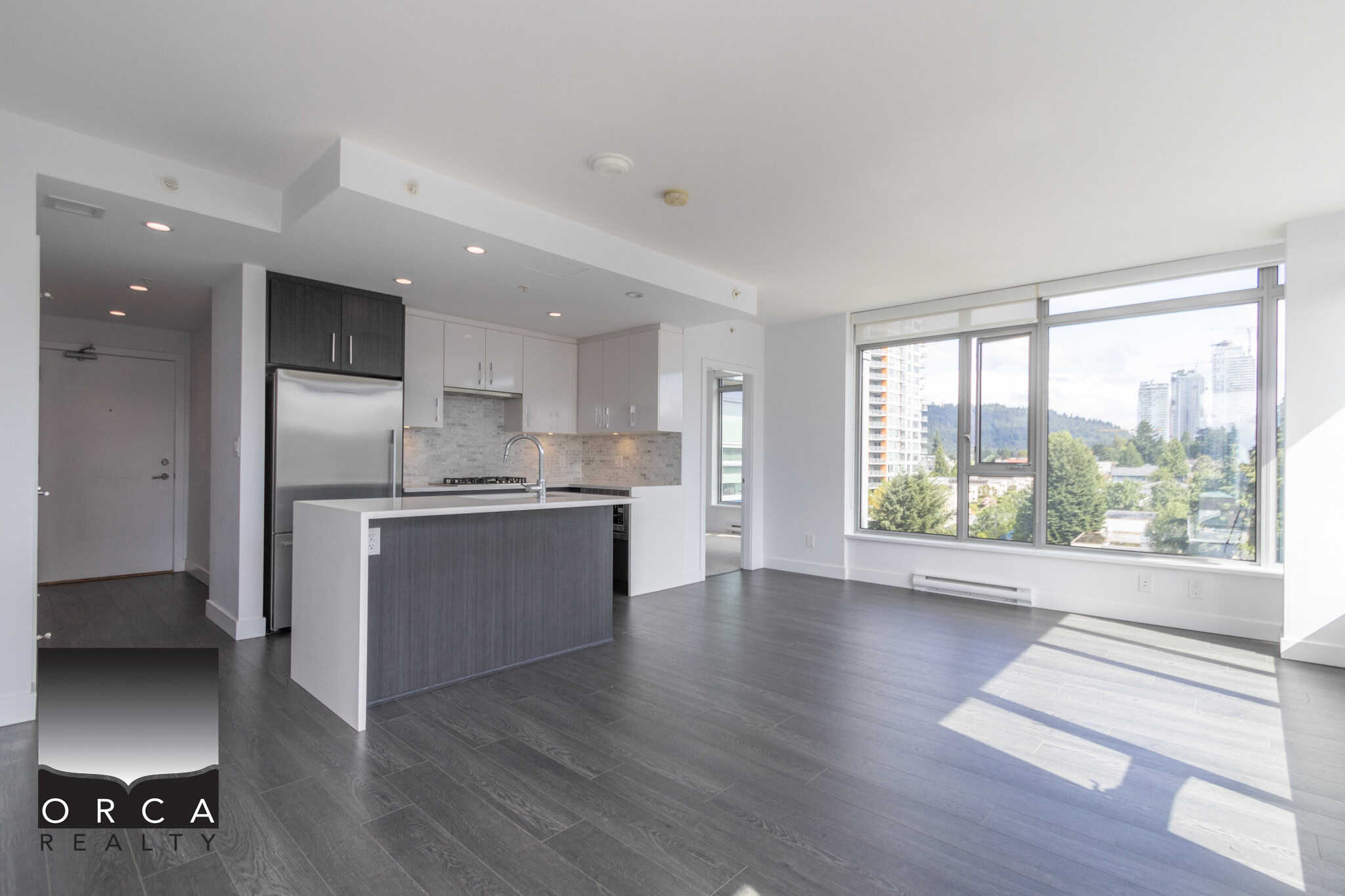 Bright modern open-concept apartment with large windows offering stunning city and mountain views, featuring stylish kitchen with stainless steel appliances, ideal for Vancouver condo living.