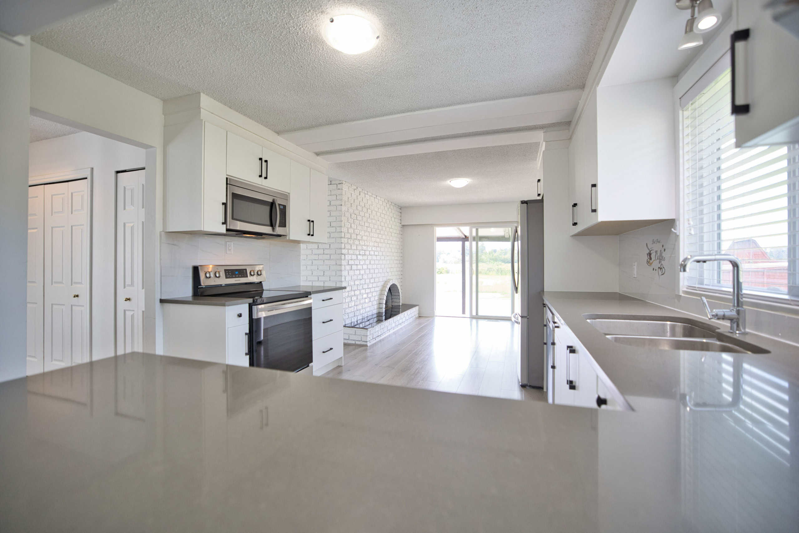 Modern white kitchen with stainless steel appliances, granite countertops, and large window; ideal for homebuyers seeking stylish, functional spaces in BC.