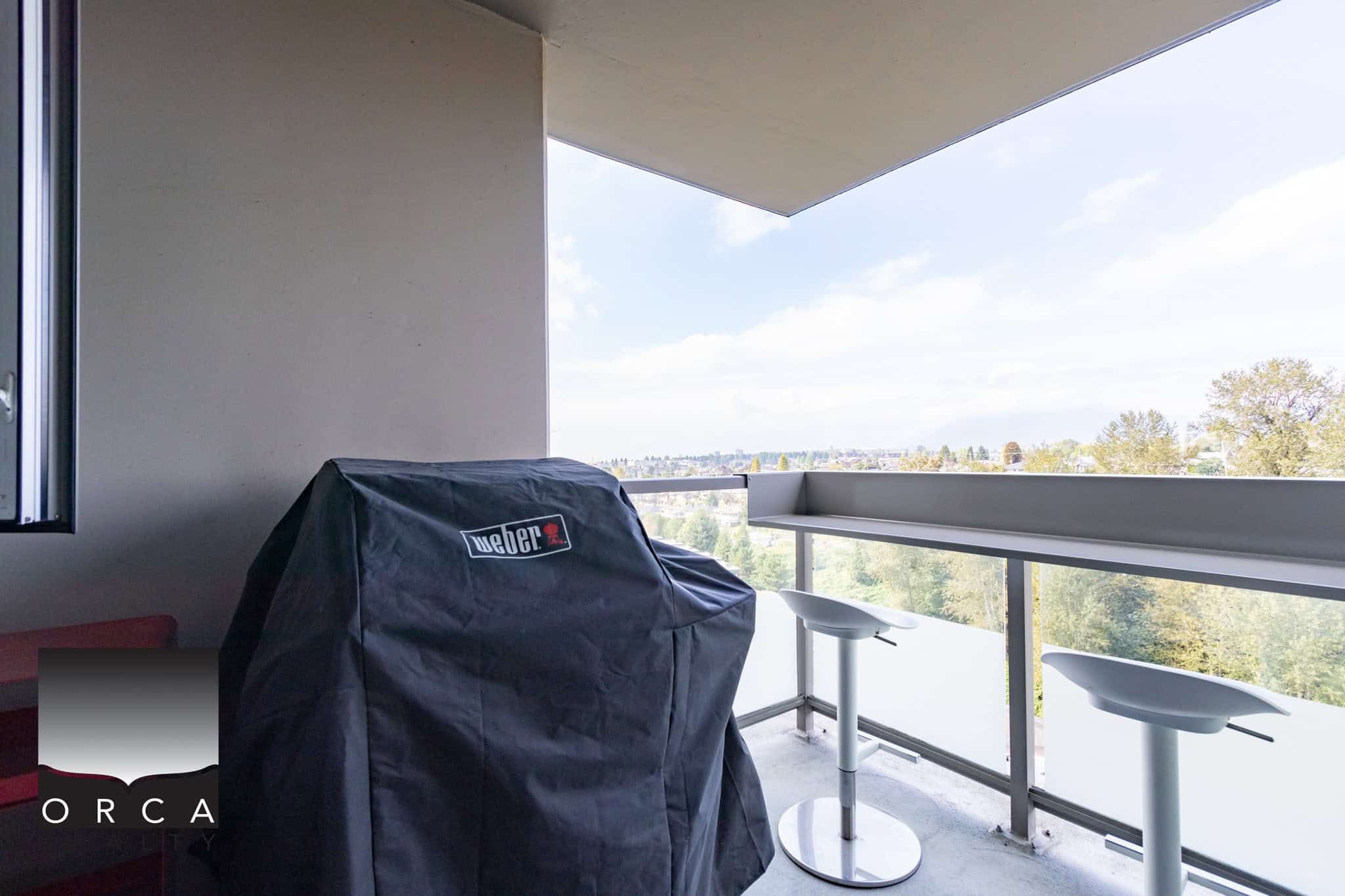 Spacious outdoor balcony with a barbecue grill, modern bar stools, and panoramic city and nature views in a Calgary condo, perfect for outdoor entertaining and relaxed living.