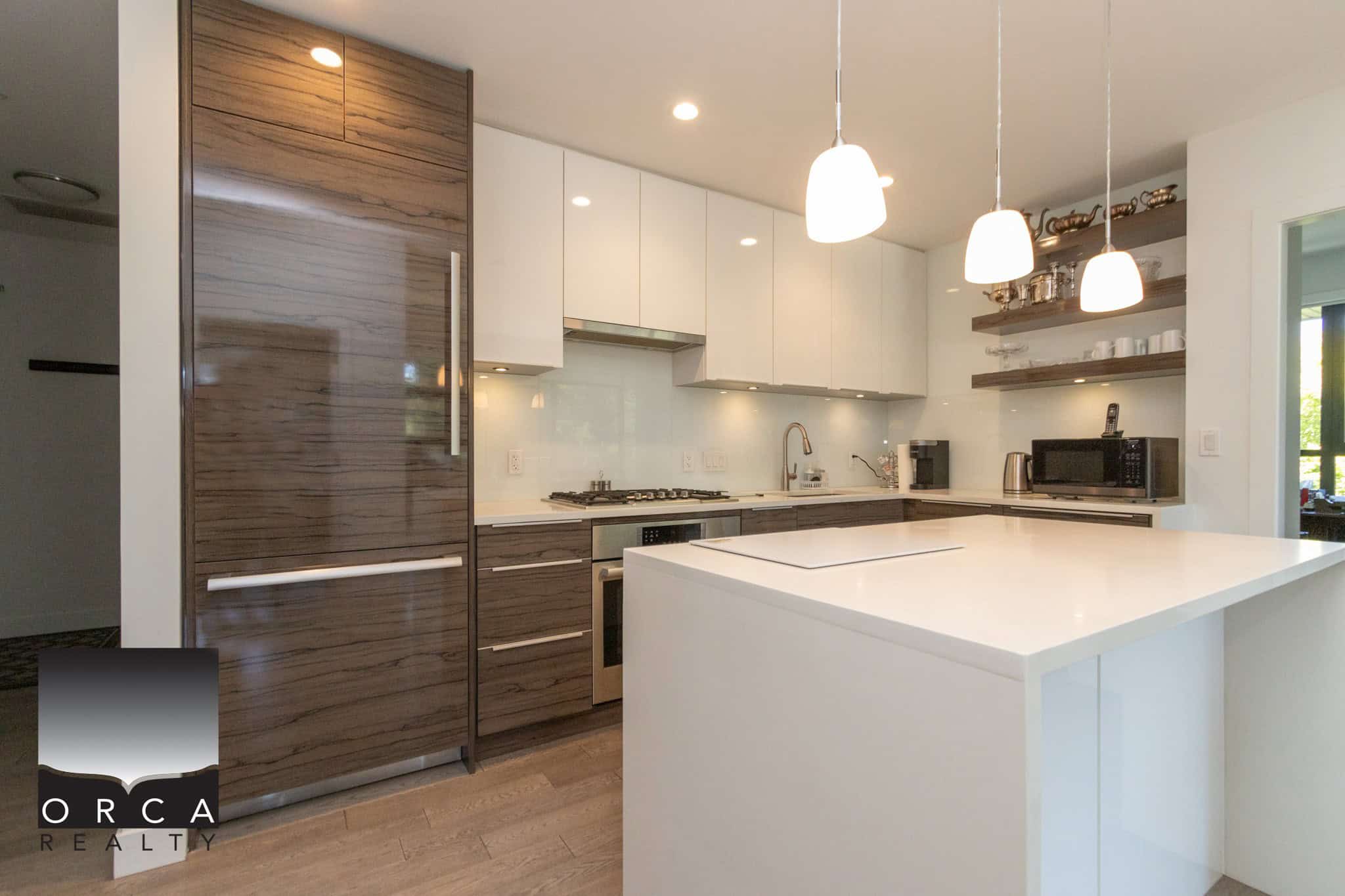 Modern kitchen with white and wood cabinetry, sleek countertops, and contemporary pendant lighting, ideal for luxury homes listed by Orca Realty Inc. in Vancouver.