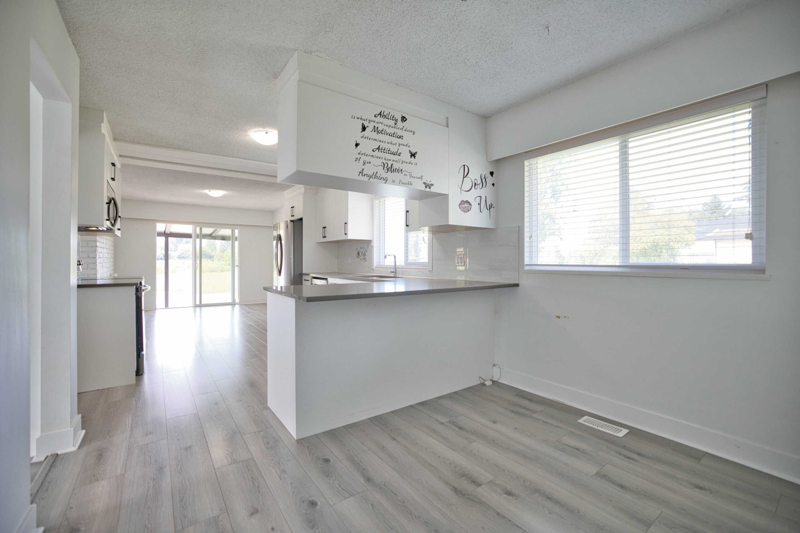 Bright white kitchen and living area with modern appliances, large windows, and personalized wall decor, ideal for Vancouver Island real estate and homebuyers seeking a stylish, move-in ready property.