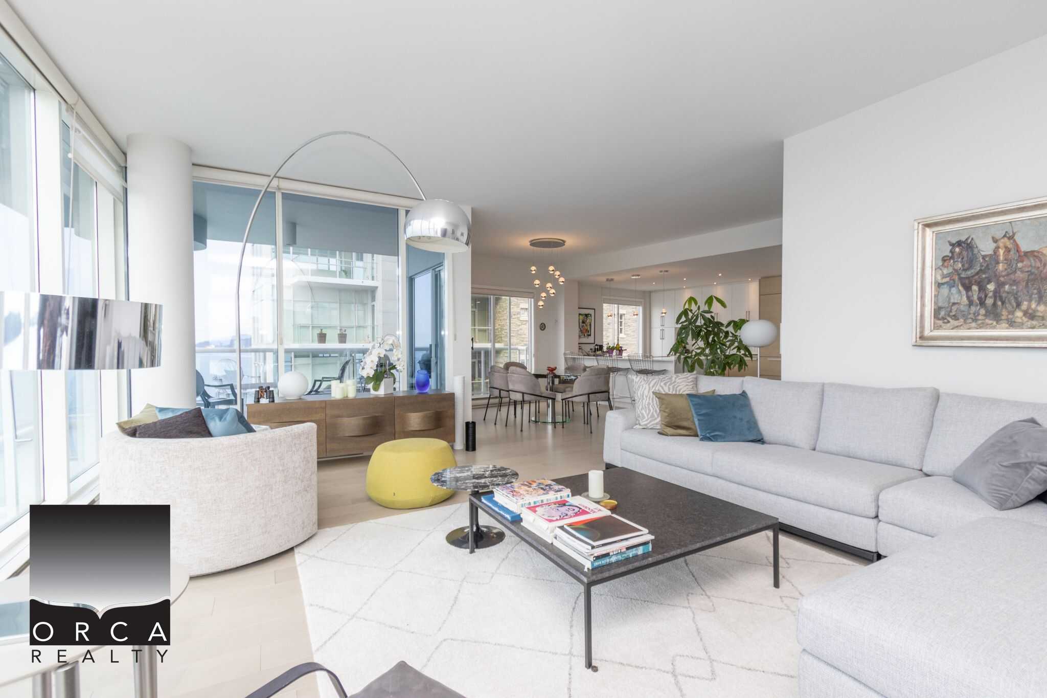 Modern open-concept living room with large windows, stylish furniture, and contemporary decor, showcasing a luxurious Vancouver waterfront condo by Orca Realty Inc.