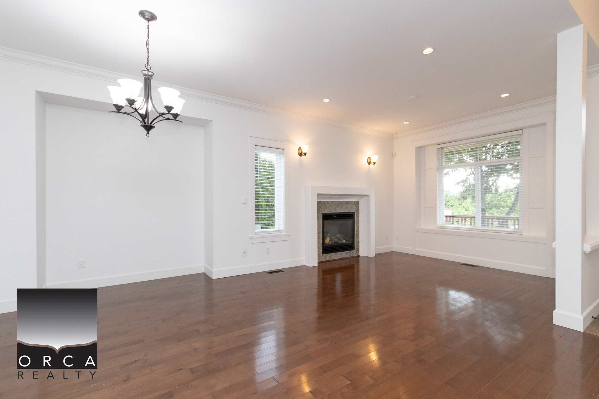 Spacious living room with hardwood floors, white walls, fireplace, large windows, and modern lighting, showcasing the elegance of Ontario homes listed by Orca Realty Inc.