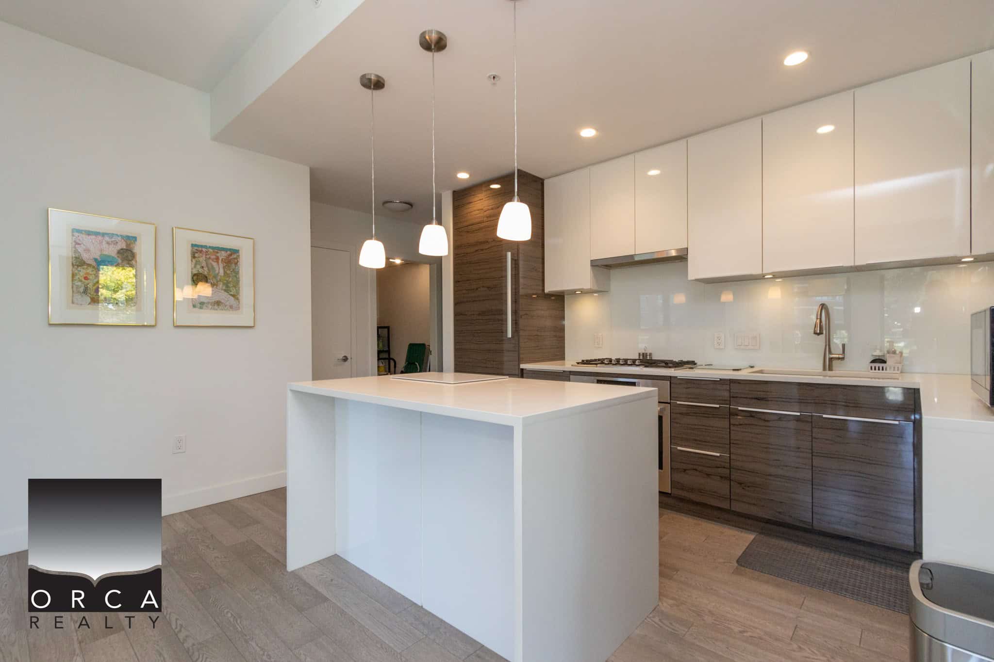 Modern kitchen featuring sleek white cabinets, dark wood accents, and a spacious island with pendant lighting, ideal for Vancouver real estate buyers seeking contemporary homes.