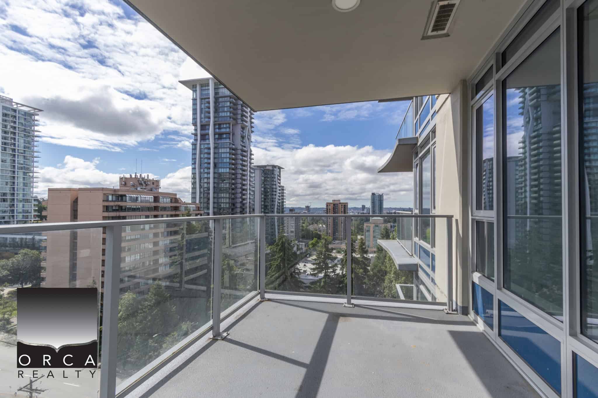 Panoramic balcony view of downtown Vancouver from a modern high-rise apartment, showcasing cityscape, glass railing, and clear blue sky, ideal for urban living in BC.