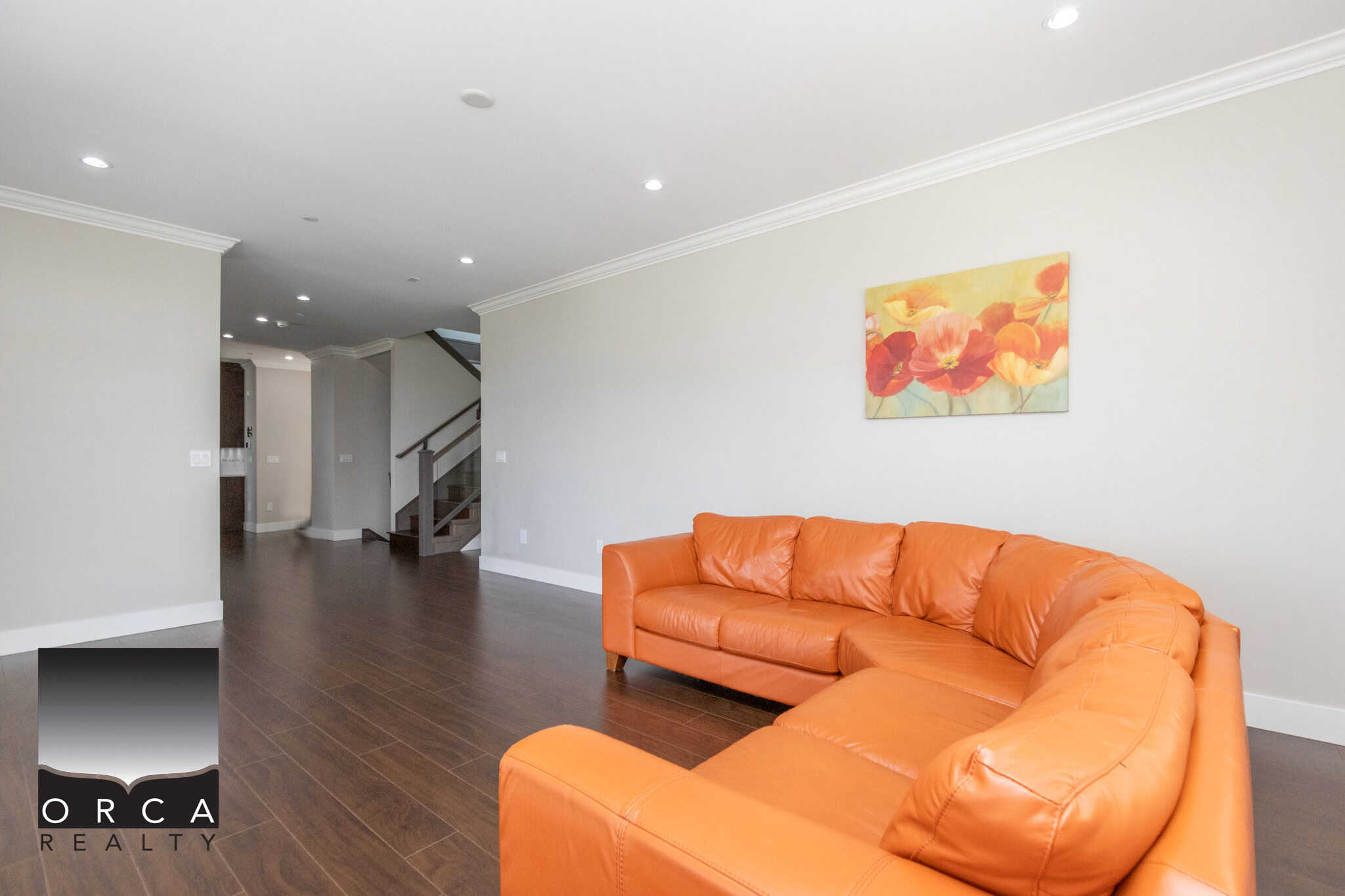 Bright and modern living room interior with an orange leather sofa, hardwood flooring, and minimalist decor, showcasing the quality real estate services of Orca Realty Inc. in Vancouver.